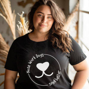 Black t-shirt with white circular text reading "Nose Work Dogs Smell Better" surrounding a heart-shaped dog nose graphic