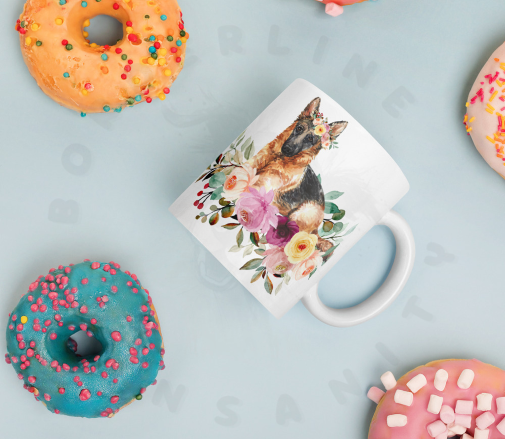 german shepherd in flowers mug lying on a blue table surrounded by colorful donuts