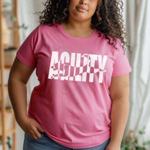 a woman in front of a boho background wearing a charity pink shirt that says agility with a leaping dog silhouette cutting through the lettering