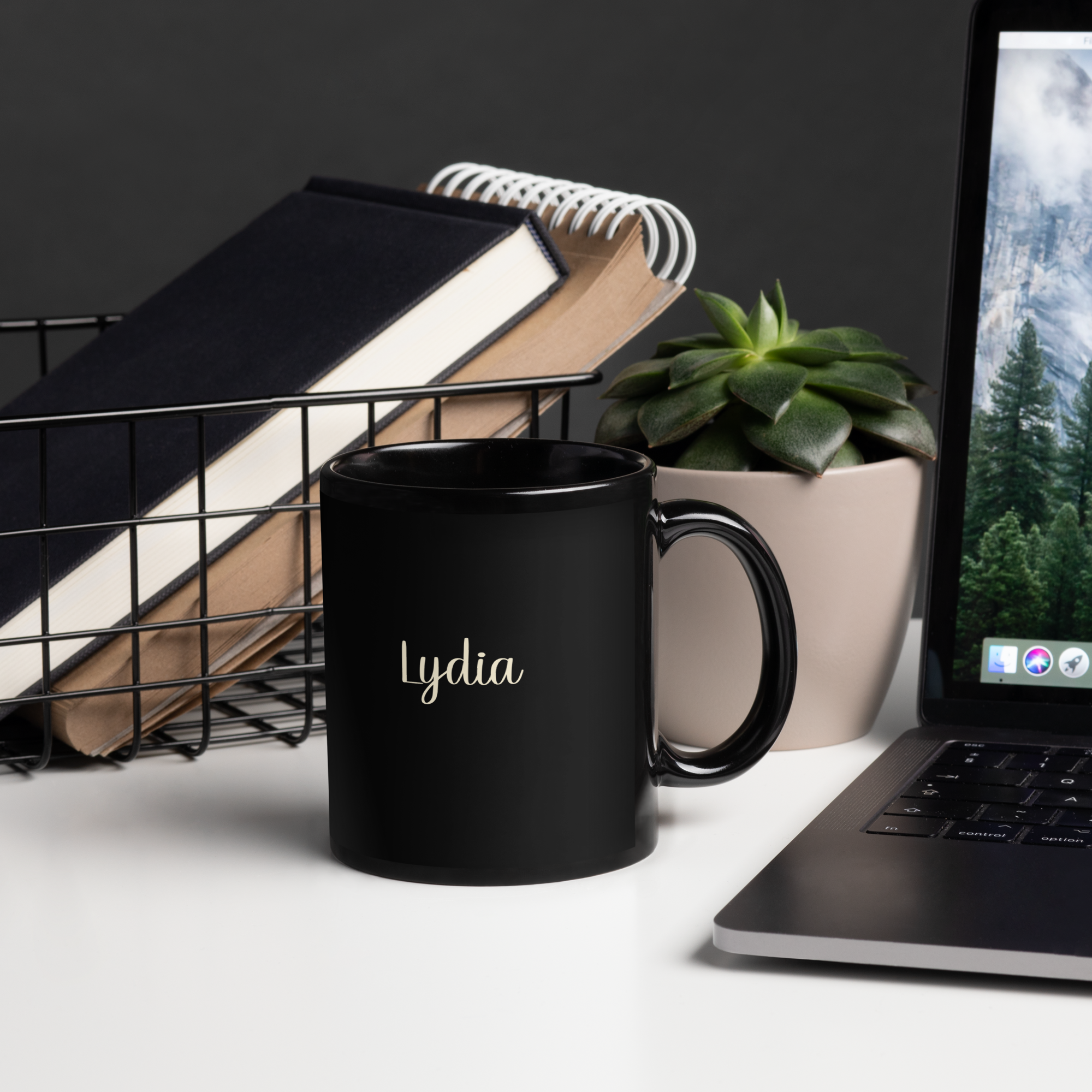 an 11 ounce black mug sitting on a desk near a laptop and books. it is personalized