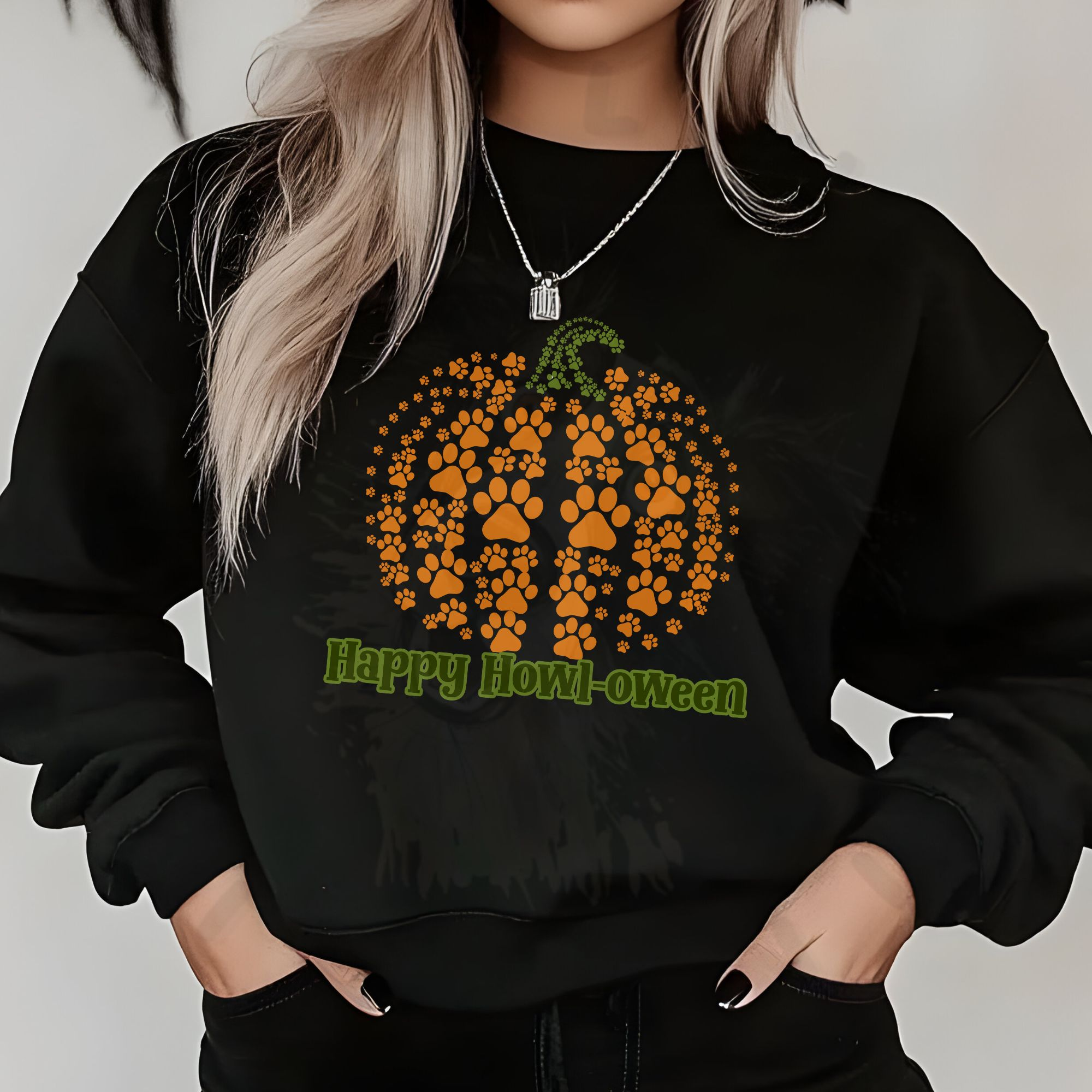 a woman standing in front of a white wall with halloween decorations wearing a black sweatshirt with a pumpkin made of pawprints and the phrase happy howl-oween