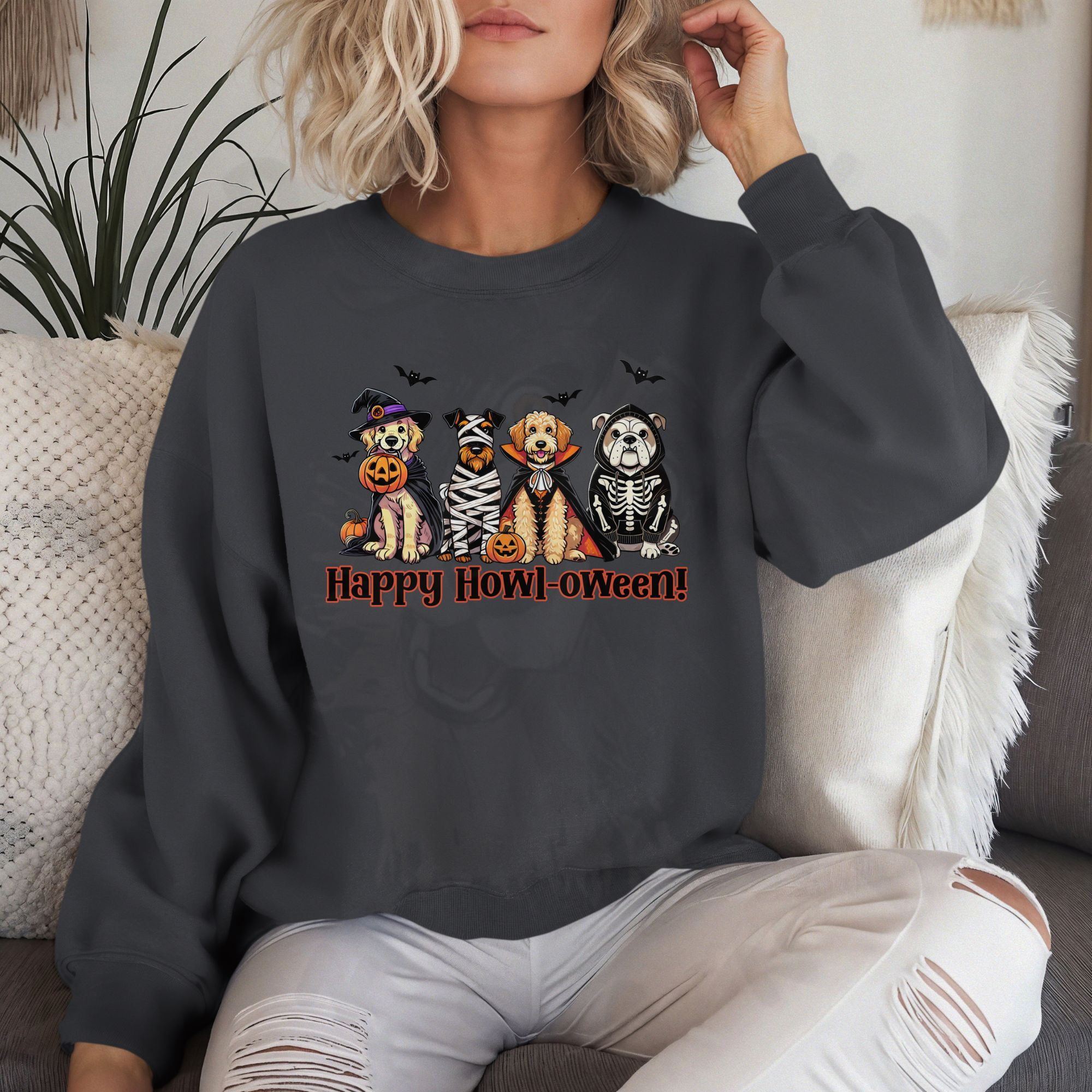 a woman on a white sofa wearing a charcoal sweatshirt with a graphic of 4 dogs in costumes with the phrase happy howl-oween