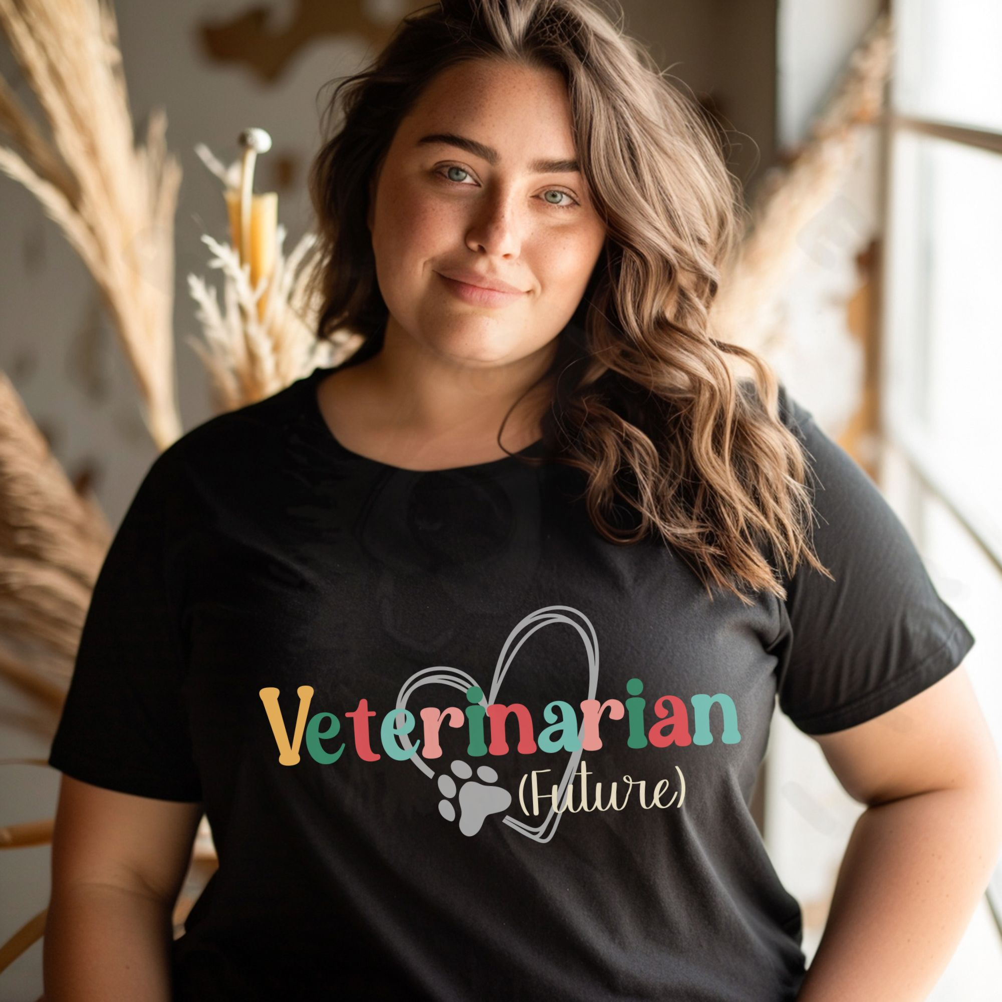 a woman standing in front of a boho background wearing a black future veterinarian tee with a heart and pawprint