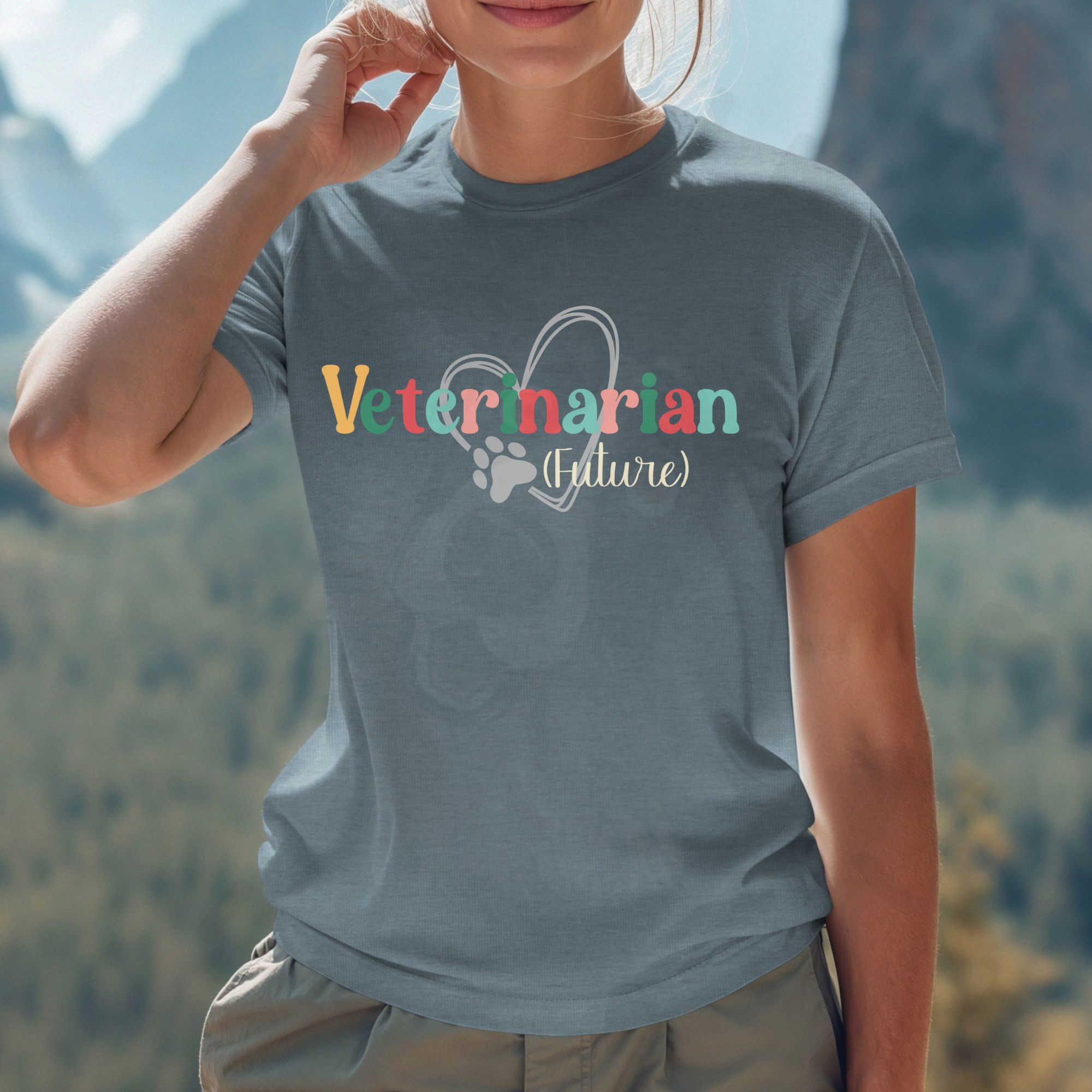 a woman standing in front of distant mountains wearing a heather slate future veterinarian tee with a heart and paw print