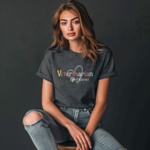 a woman sitting on a stool in front of a dark gray background wearing ripped jeans and a dark gray heather future veterinarian tee with a heart and paw print