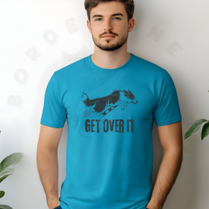 a man standing against a wall between plants wearing an aqua get over it tee with a border collie jumping over a bar