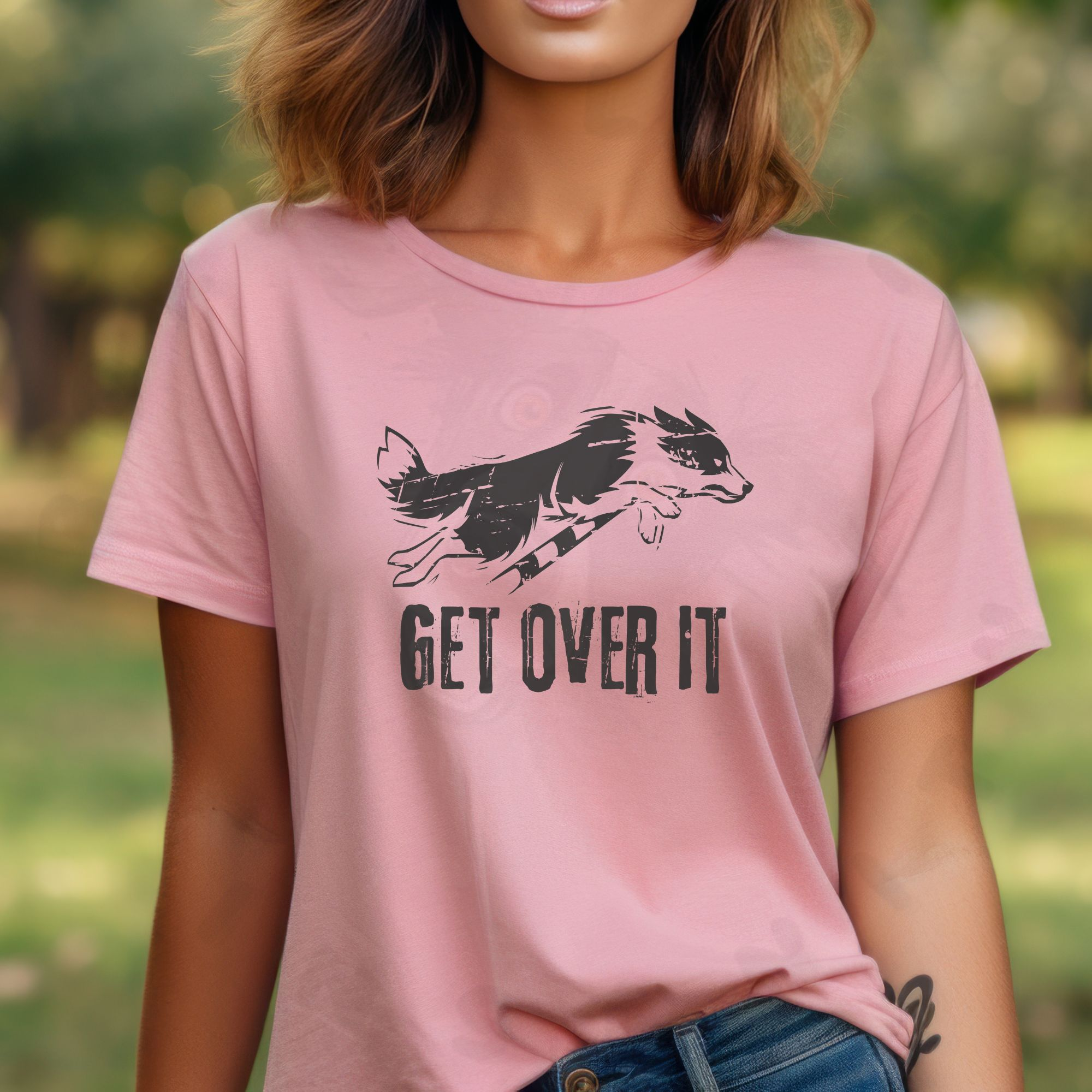 A woman in a park wearing a pink get over it tee with a border collie jumping over a bar