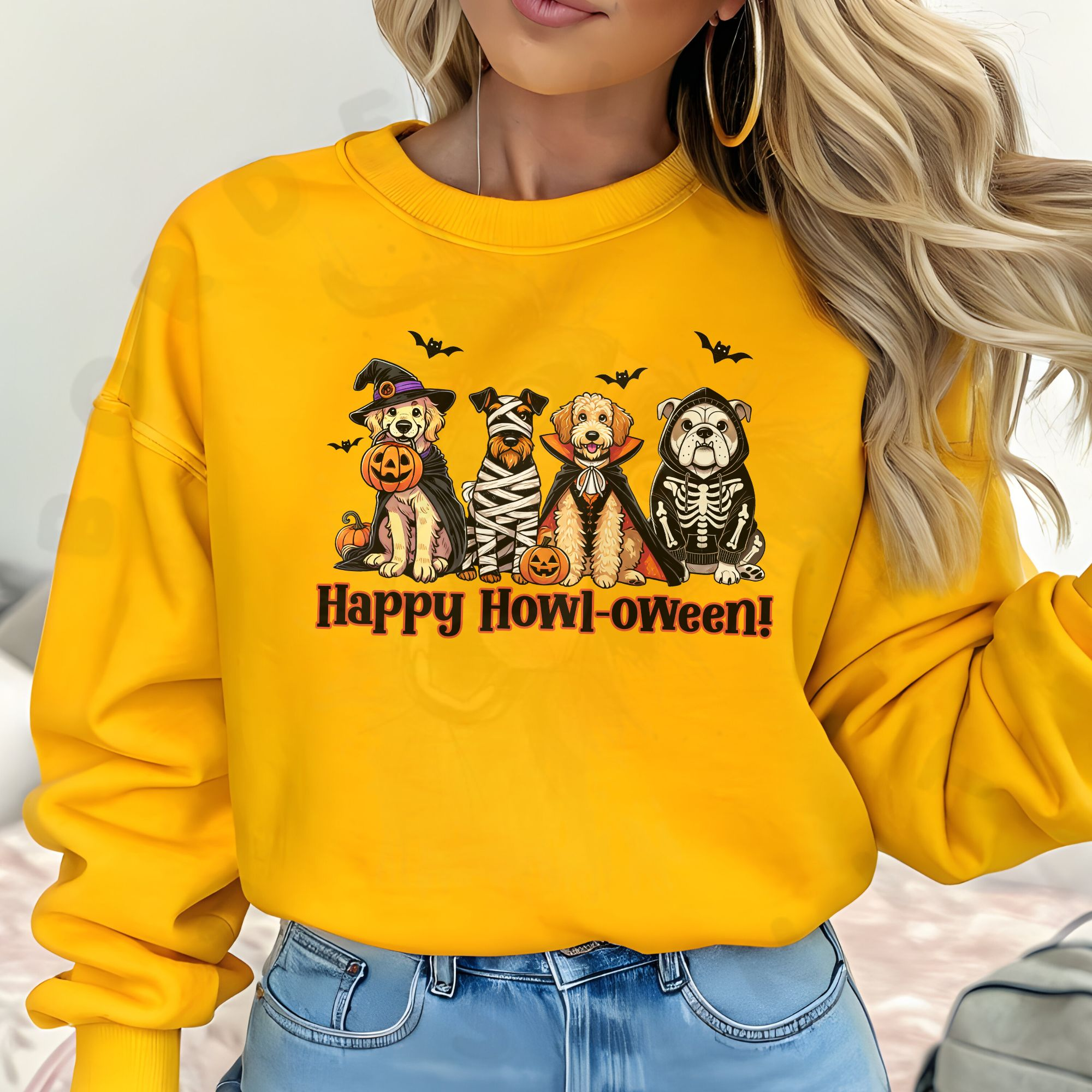 a blond woman in front of a bed wearing a gold sweatshirt with a graphic of 4 dogs wearing halloween costumes and the phrase happy howl-oween