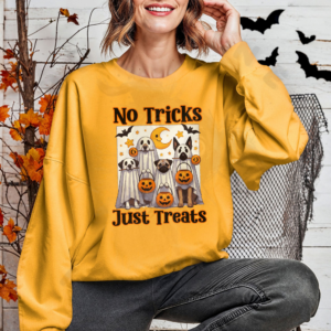 a woman in front of a halloween background wearing a gold sweatshirt with a graphic of dogs dressed as ghosts among jack-o-lanterns and the phrase no tricks just treats