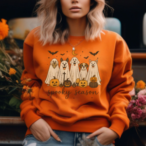 a woman leaning on a truck bed wearing a orange halloween sweatshirt that features 5 dogs dressed as ghosts with a crescent moon, jack-o-lanterns, and bats that says spooky season in cursive