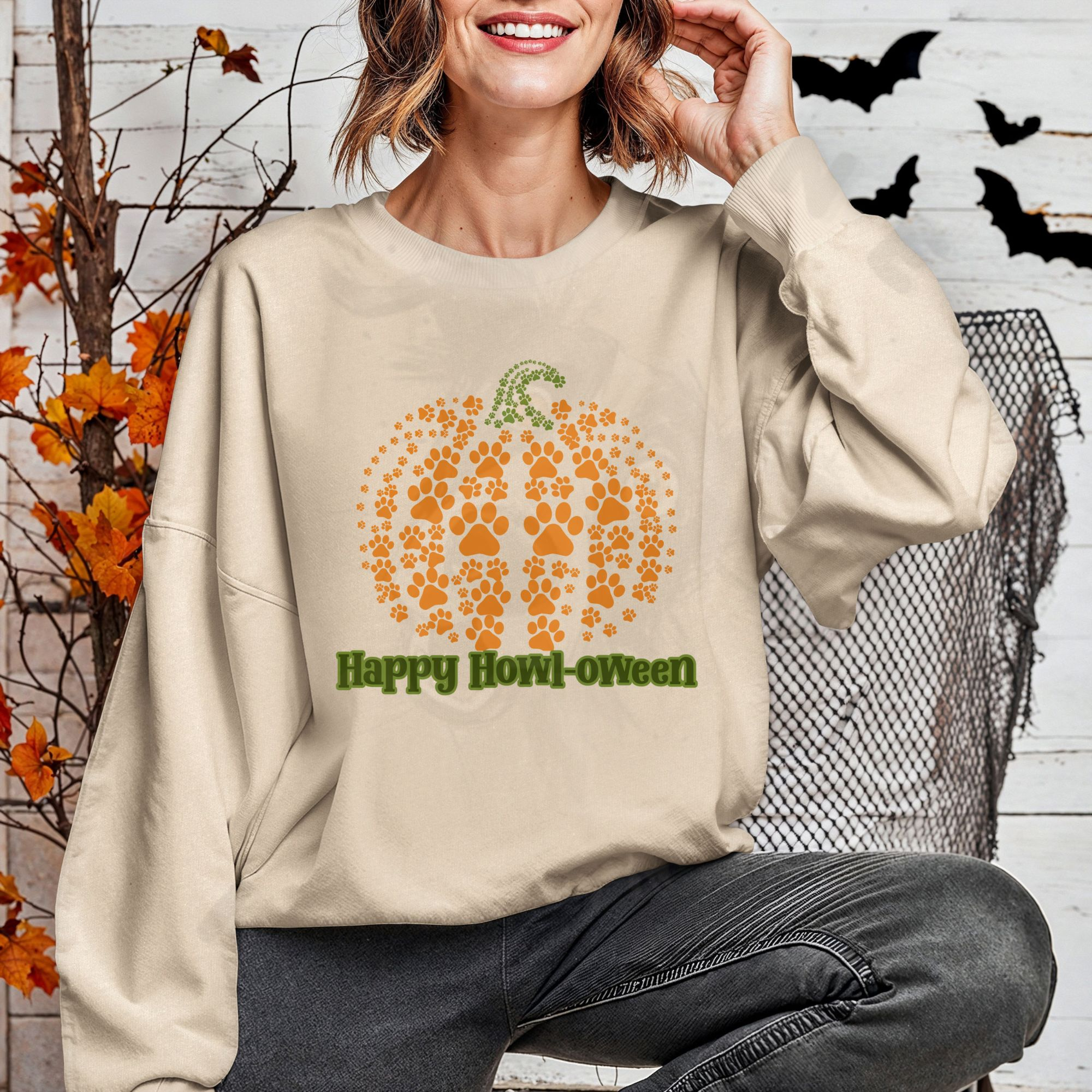 a woman in front of a halloween background wearing a sand colored sweatshirt that says happy howl-oween with a pumpkin made of pawprints above it