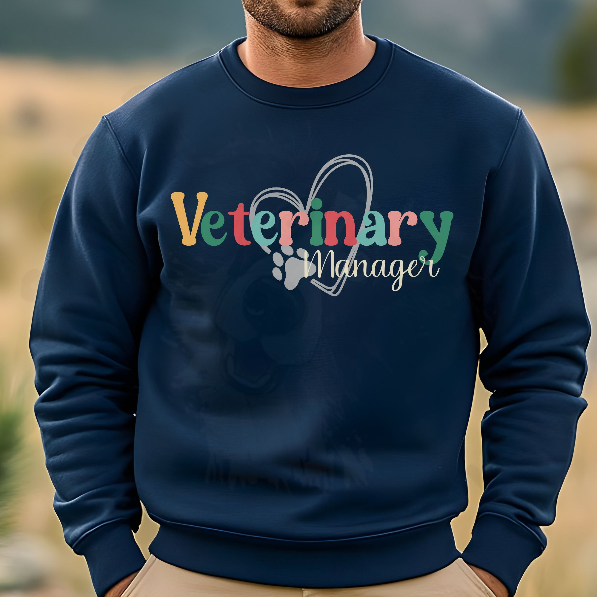 a man standing in a field wearing a navy sweatshirt with a colorful veterinary manager design with a heart and pawprint