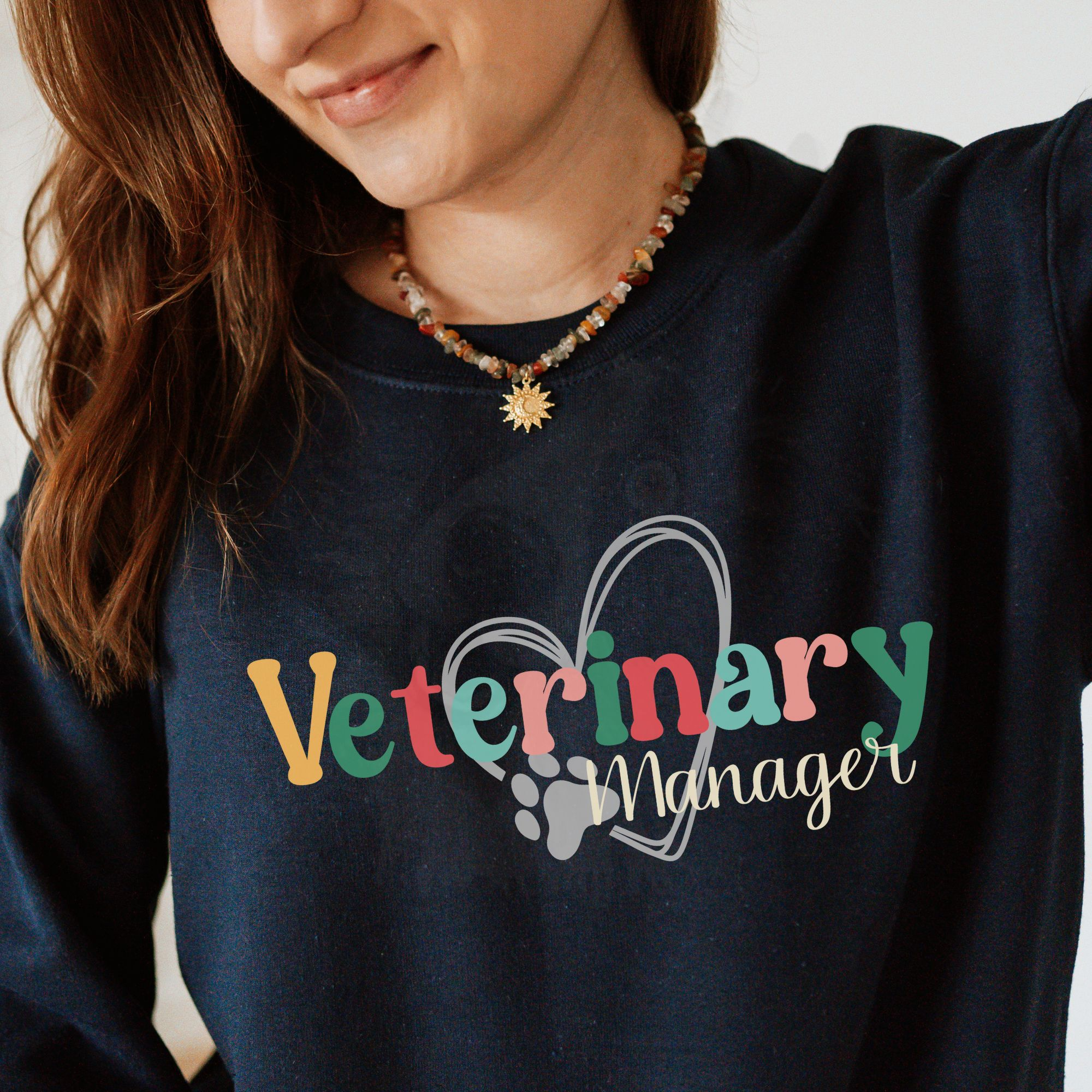 a woman wearing a navy sweatshirt with a colorful veterinary manager design with a heart and pawprint