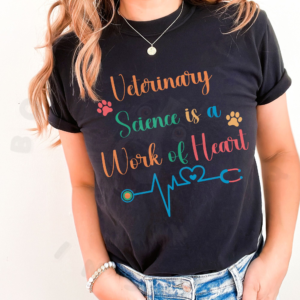 a woman in front of a white background with her hands in her pockets, wearing a black veterinary science is a work of heart t-shirt