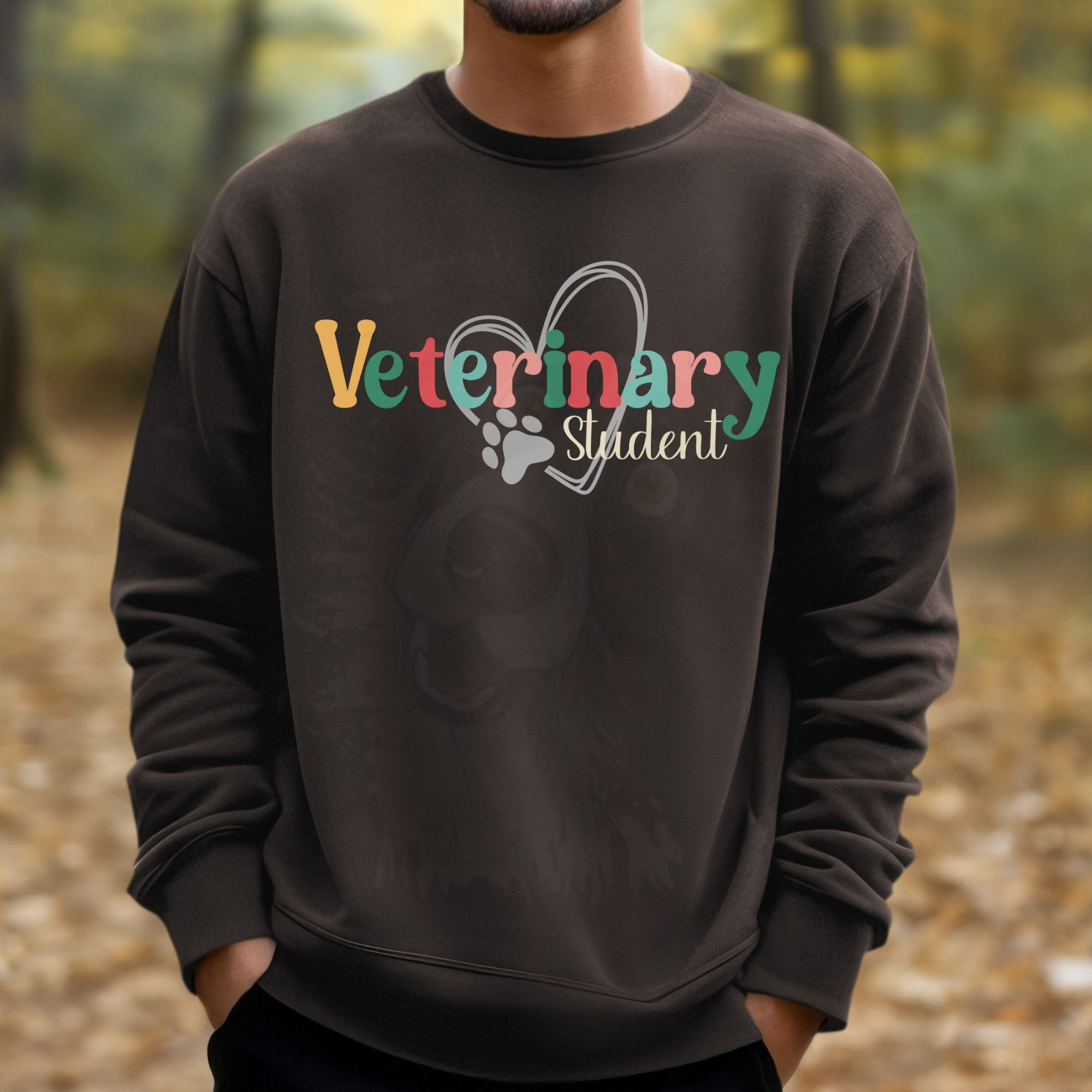 a man standing in a woods wearing a brown sweatshirt with a colorful veterinary student design with a heart and pawprint