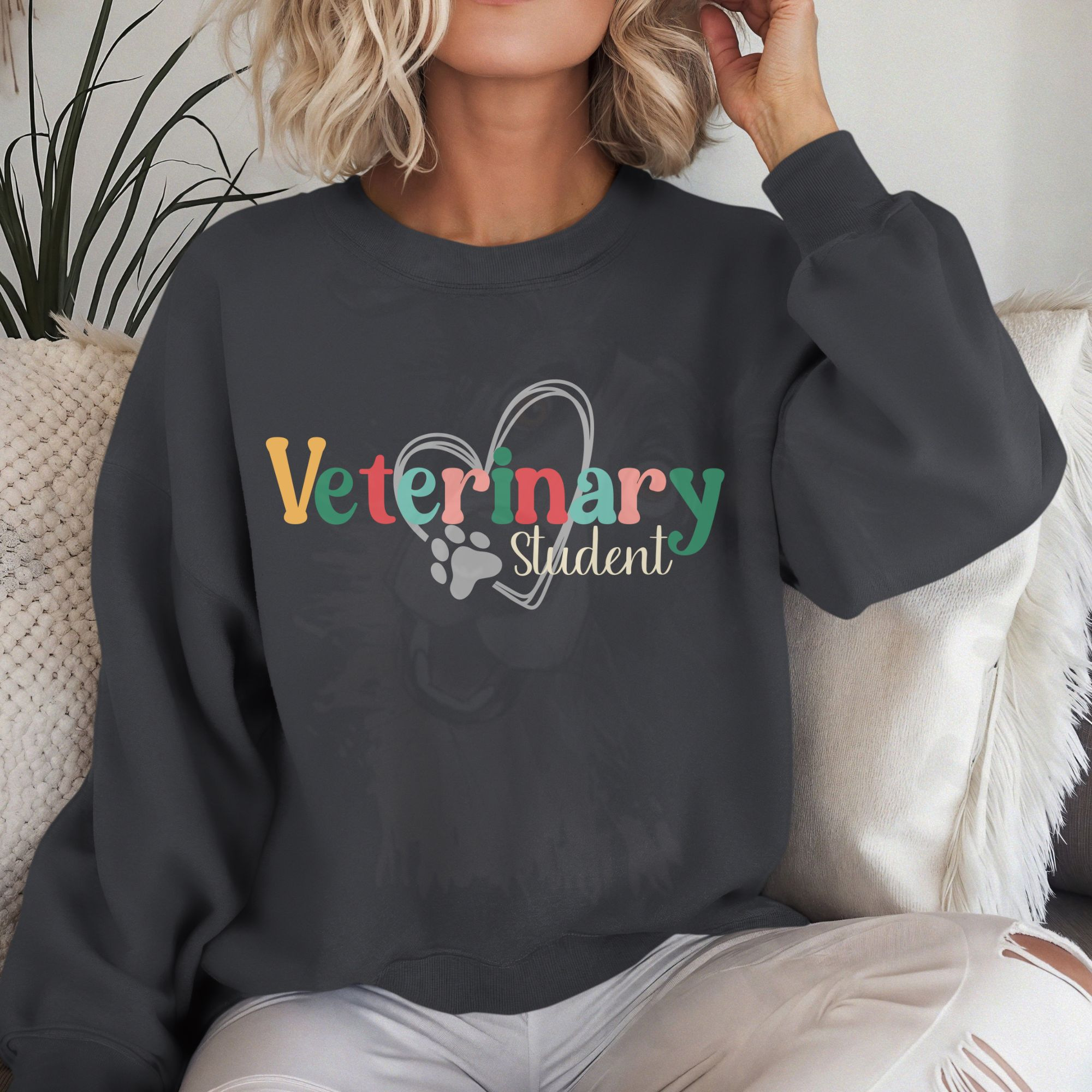 a woman on a white sofa wearing a charcoal sweatshirt with a colorful veterinary student design with a heart and pawprint