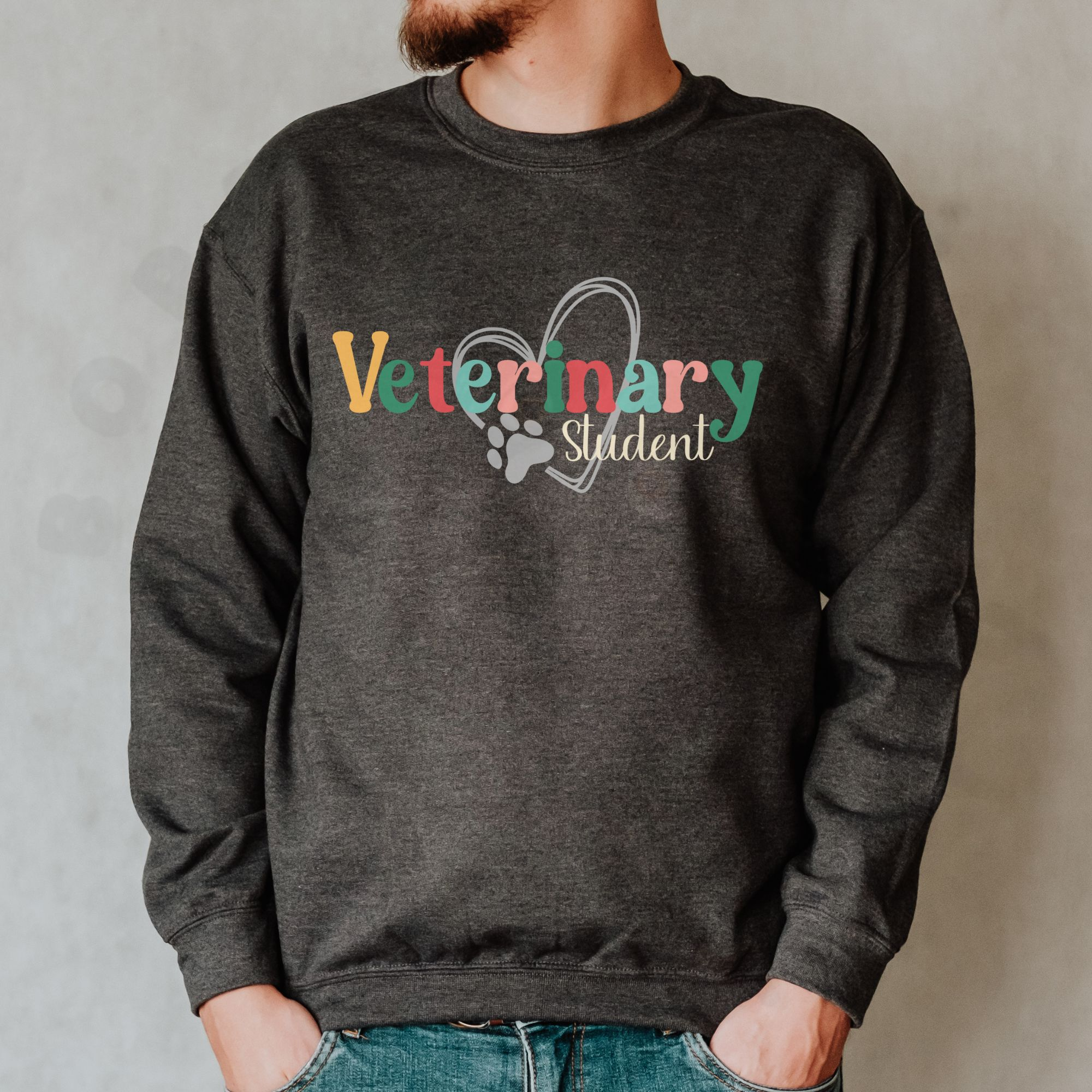 a man in front of a white background wearing a dark gray heather sweatshirt with a colorful veterinary student design with a heart and pawprint