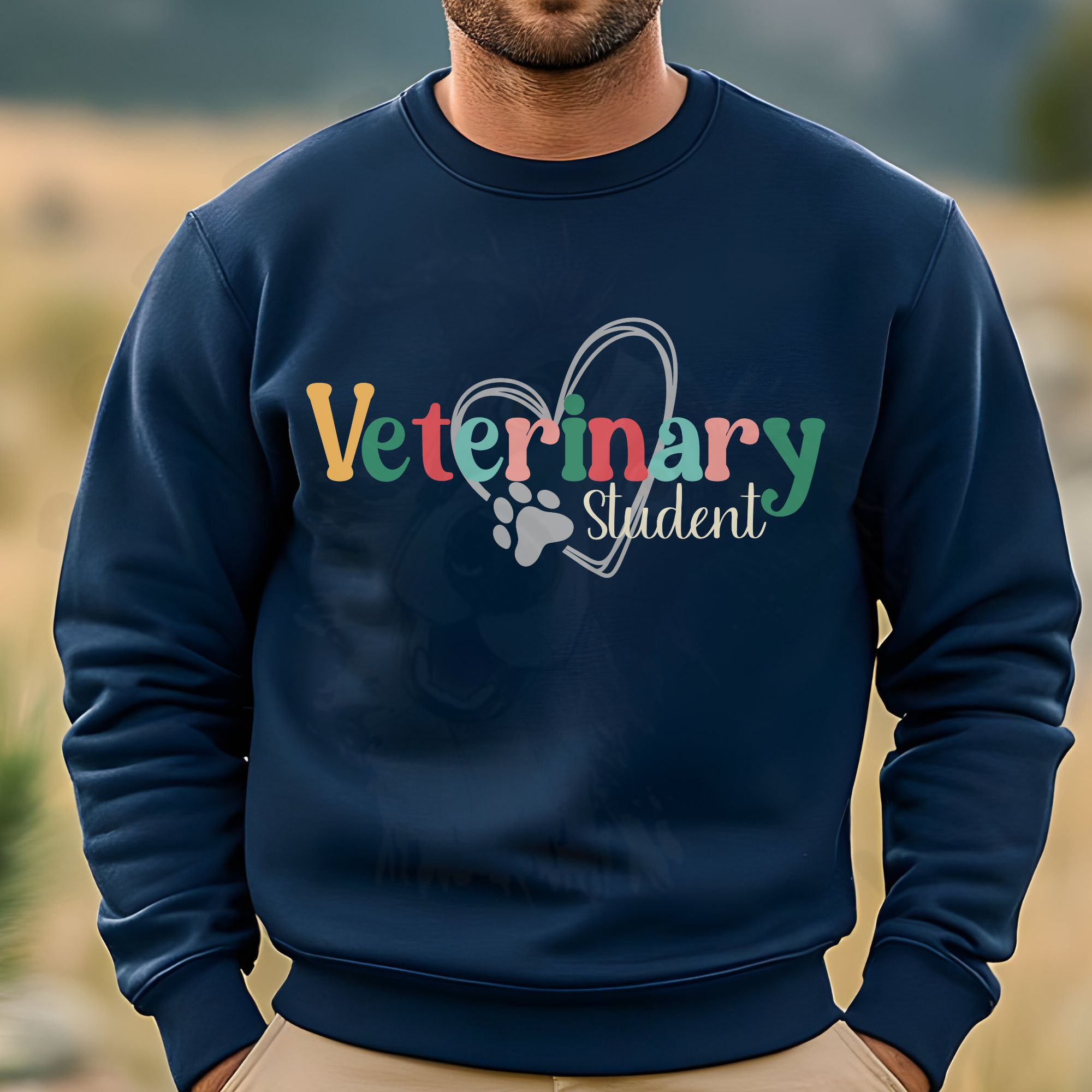 a man standing in a field wearing a navy sweatshirt with a colorful veterinary student design with a heart and pawprint