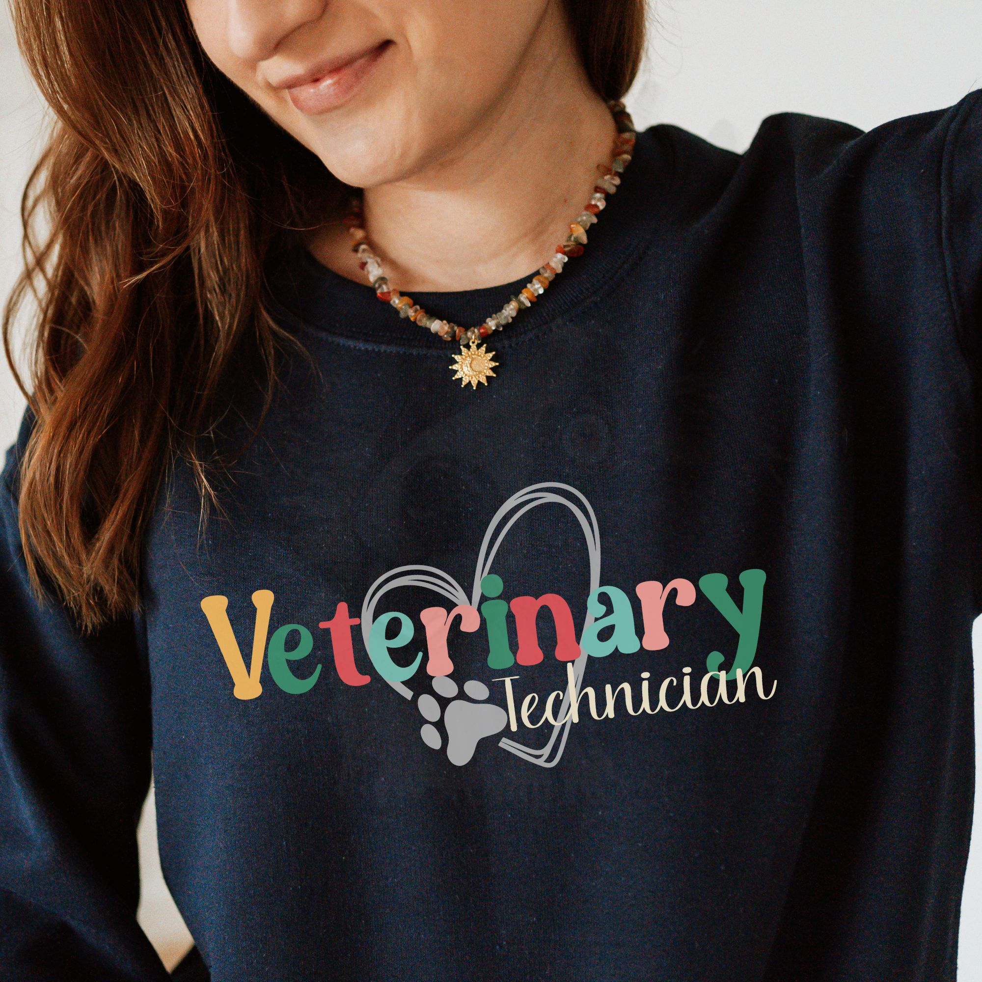 a woman wearing a navy sweatshirt with a colorful veterinary technician design with a heart and pawprint