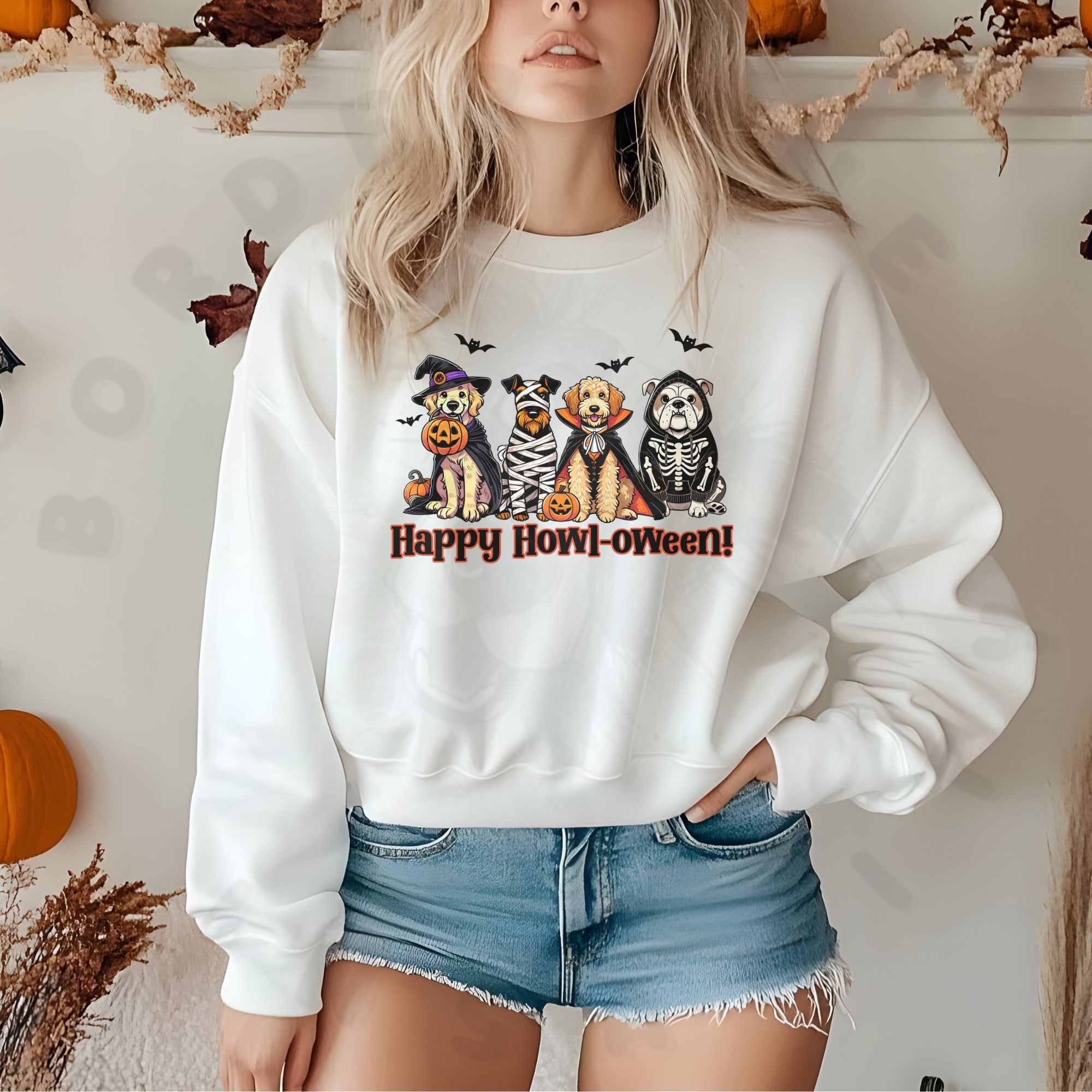 a woman standing in front of a white background with halloween decorations wearing a white sweatshirt with a graphic of 4 dogs wearing Halloween costumes with the phrase happy howl-oween