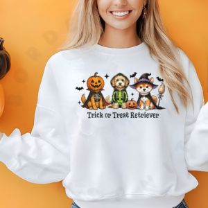 a woman in front of an orange background wearing a white trick or treat retriever sweatshirt with a graphic of 3 dogs wearing halloween costumes