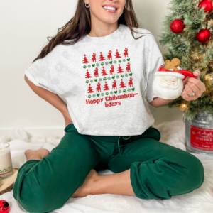 a woman sitting on the floor holding a santa mug next to a christmas tree wearing an ash grey t-shirt designed ugly christmas sweater style with rows of red christmas trees, green snowflakes, and chihuahuas wearing santa hats.