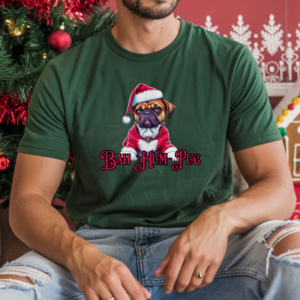 a man sitting in front of christmas decorations wearing a forest green t-shirt that says bah hum-pug below a graphic of a grumpy pug wearing a santa suit