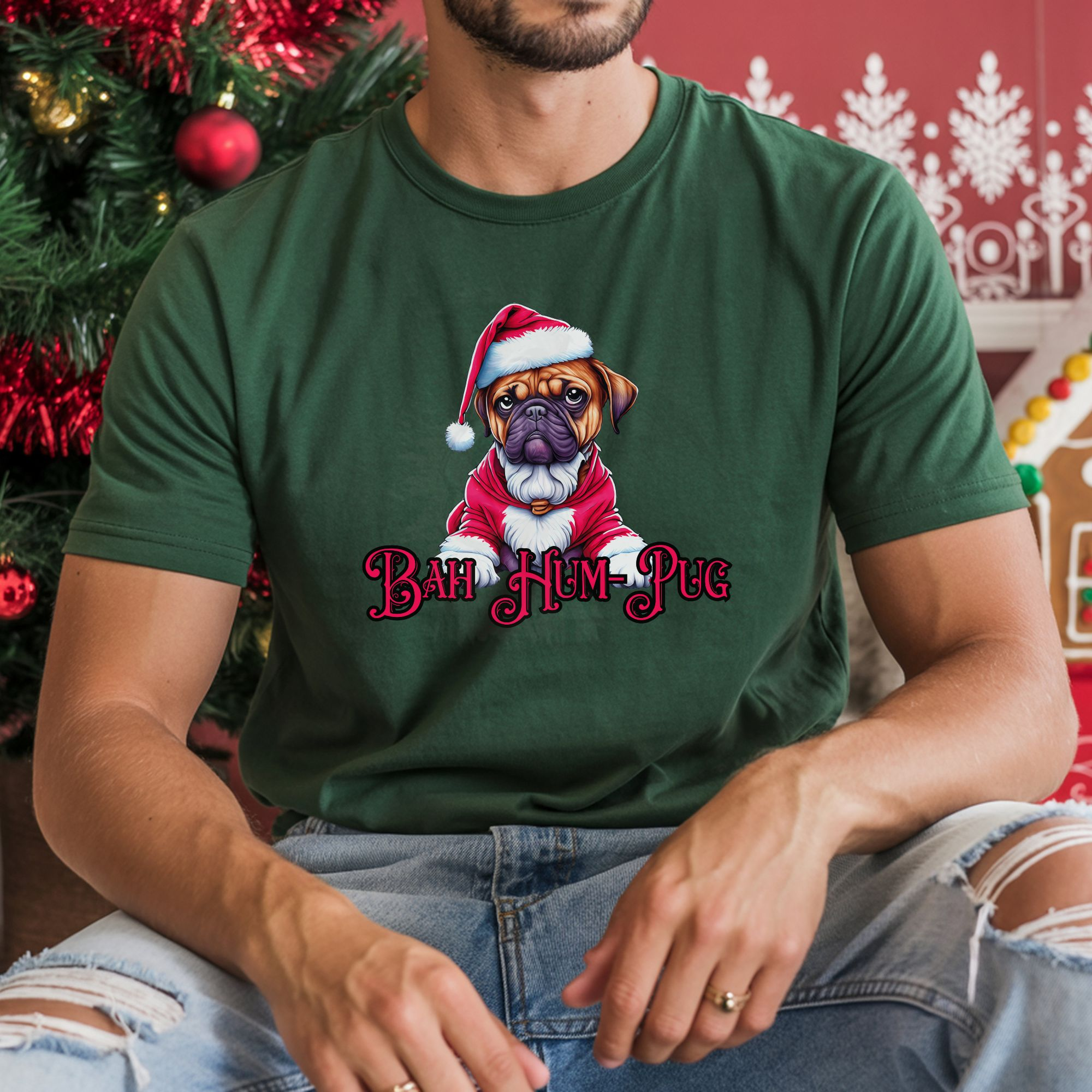 a man sitting in front of christmas decorations wearing a forest green t-shirt that says bah hum-pug below a graphic of a grumpy pug wearing a santa suit