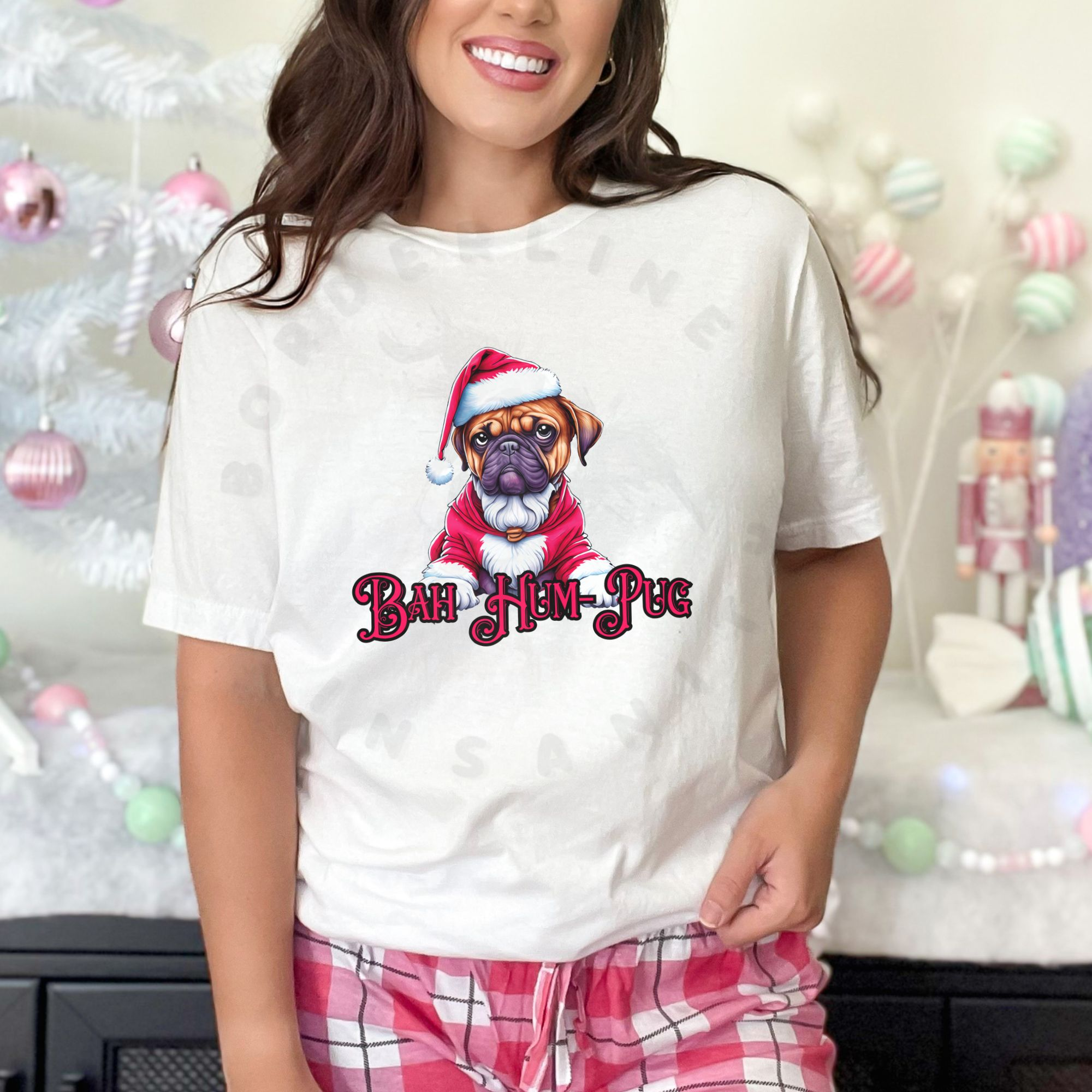a woman in pink plaid pajama pants in front of a pastel christmas background wearing a white t-shirt that says bah hum-pug below a graphic of a grumpy pug wearing a santa suit