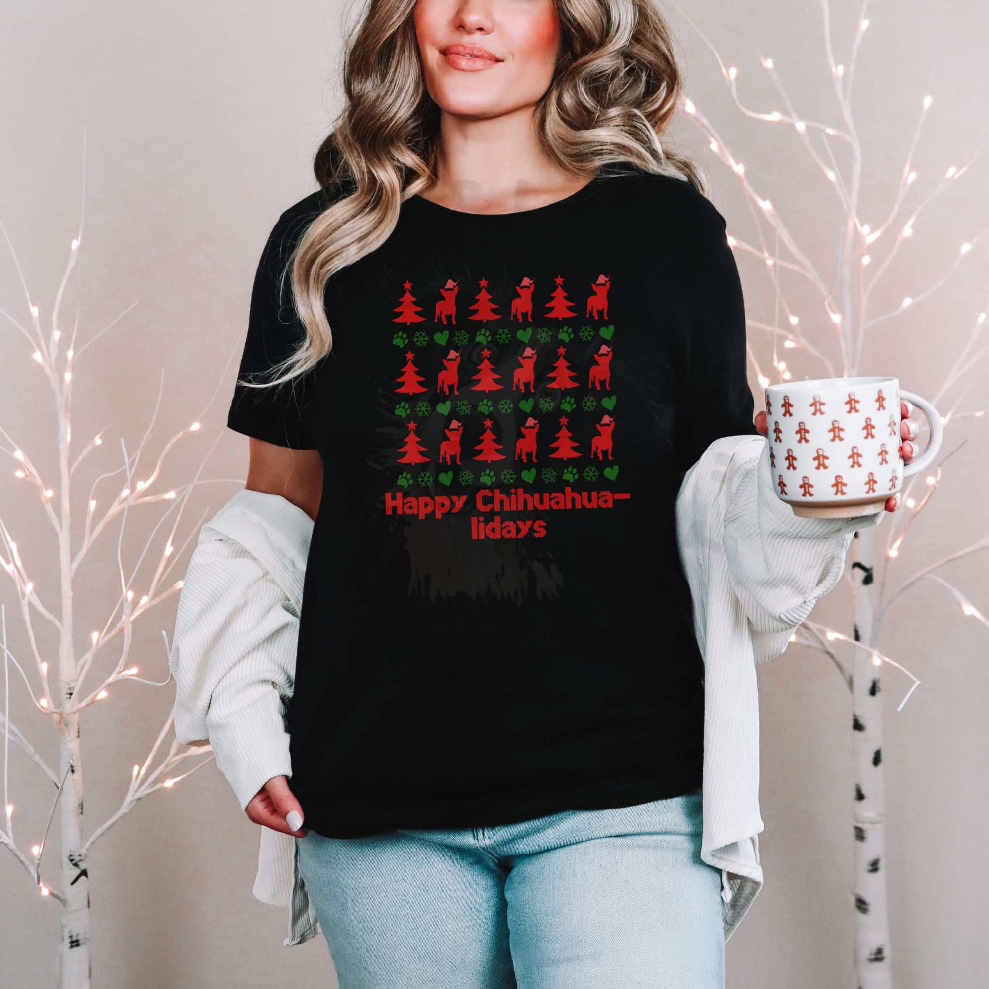 a woman standing in front of a christmas background holding a holiday mug wearing a black t-shirt designed ugly christmas sweater style with rows of red christmas trees, green snowflakes, and chihuahuas wearing santa hats.