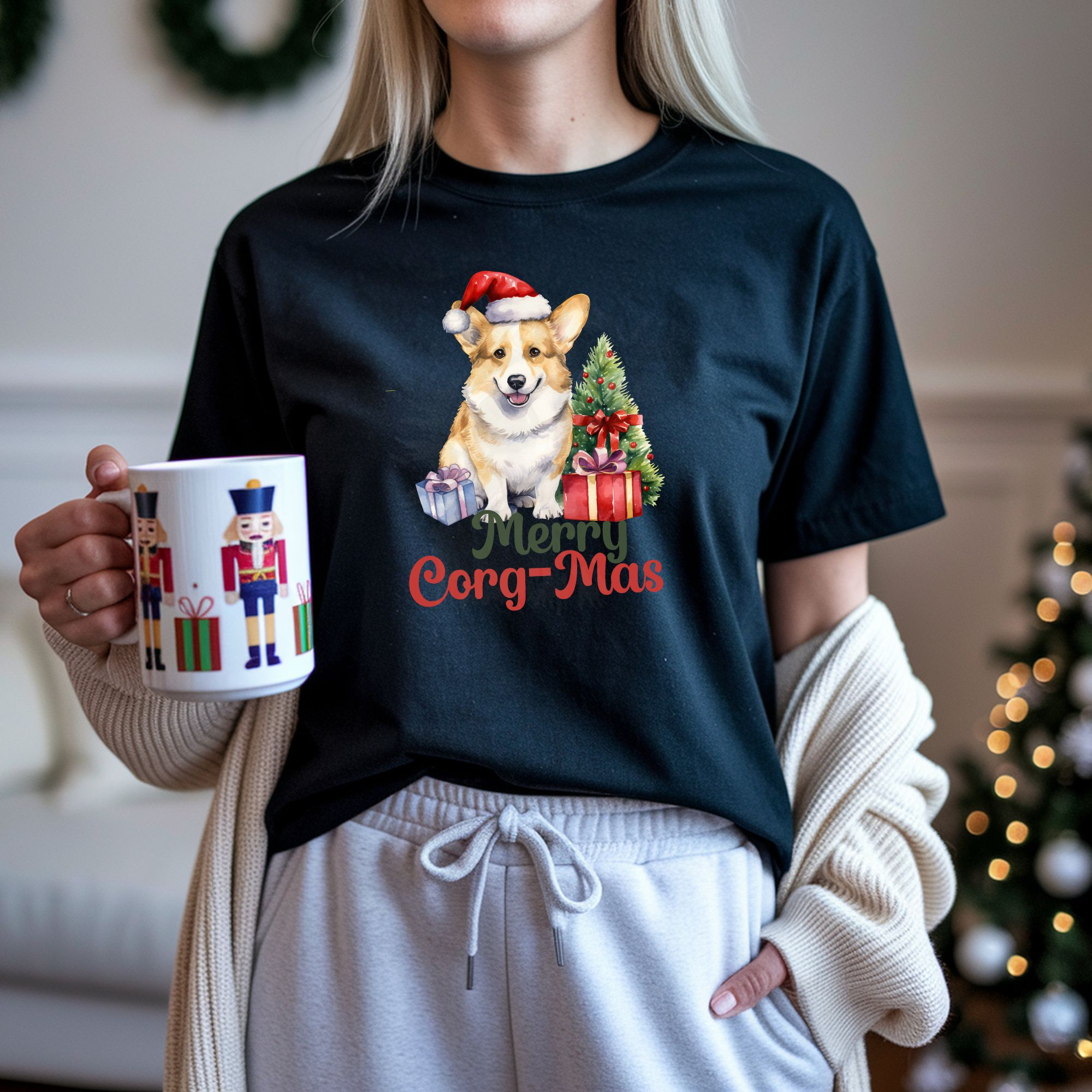 a woman holding a nutcracker mug wearing a black t-shirt with a graphic of a corgi in a Santa hat with a Christmas tree and gifts that says Merry Corg-mas