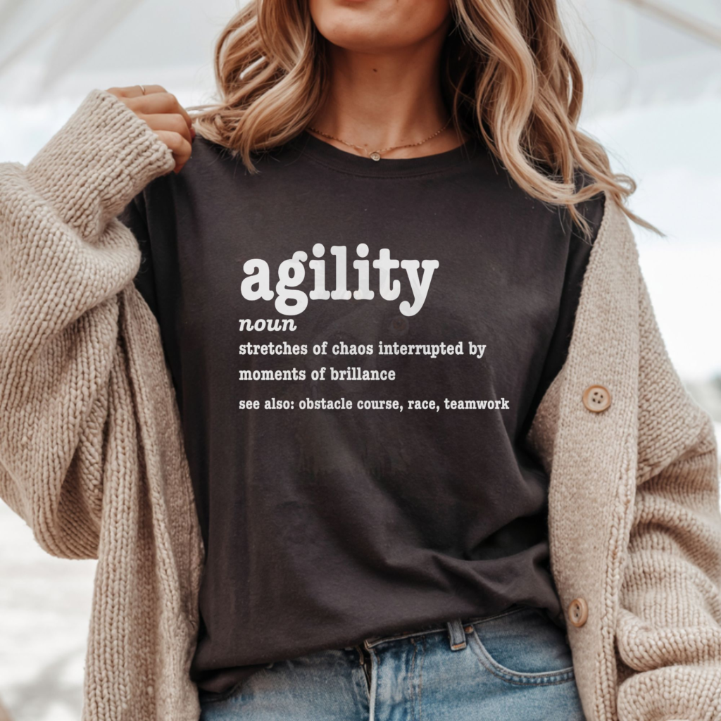 a woman wearing a tan sweater over a brown tee featuring a humorous agility definition