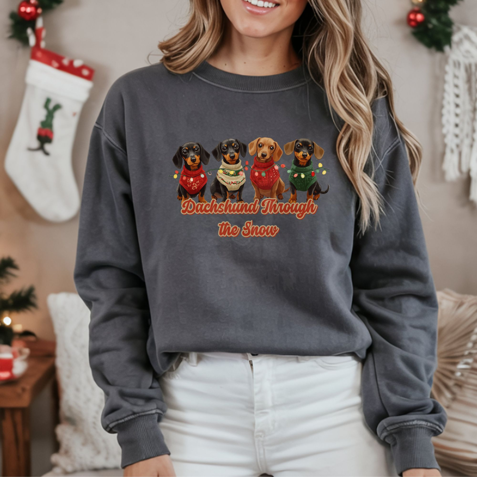 a christmas background with stockings with a woman wearing a charcoal dachshund through the snow sweatshirt featuring 4 dachshunds wearing christmas sweaters and tangled in christmas lights
