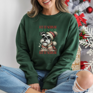 a woman in jeans ripped at the knee sitting in front of a christmas tree wearing a forest green sweatshirt that features a schnauzer wearing a festive winter hat and scarf and the words let it schnau let it schnau let it schnau