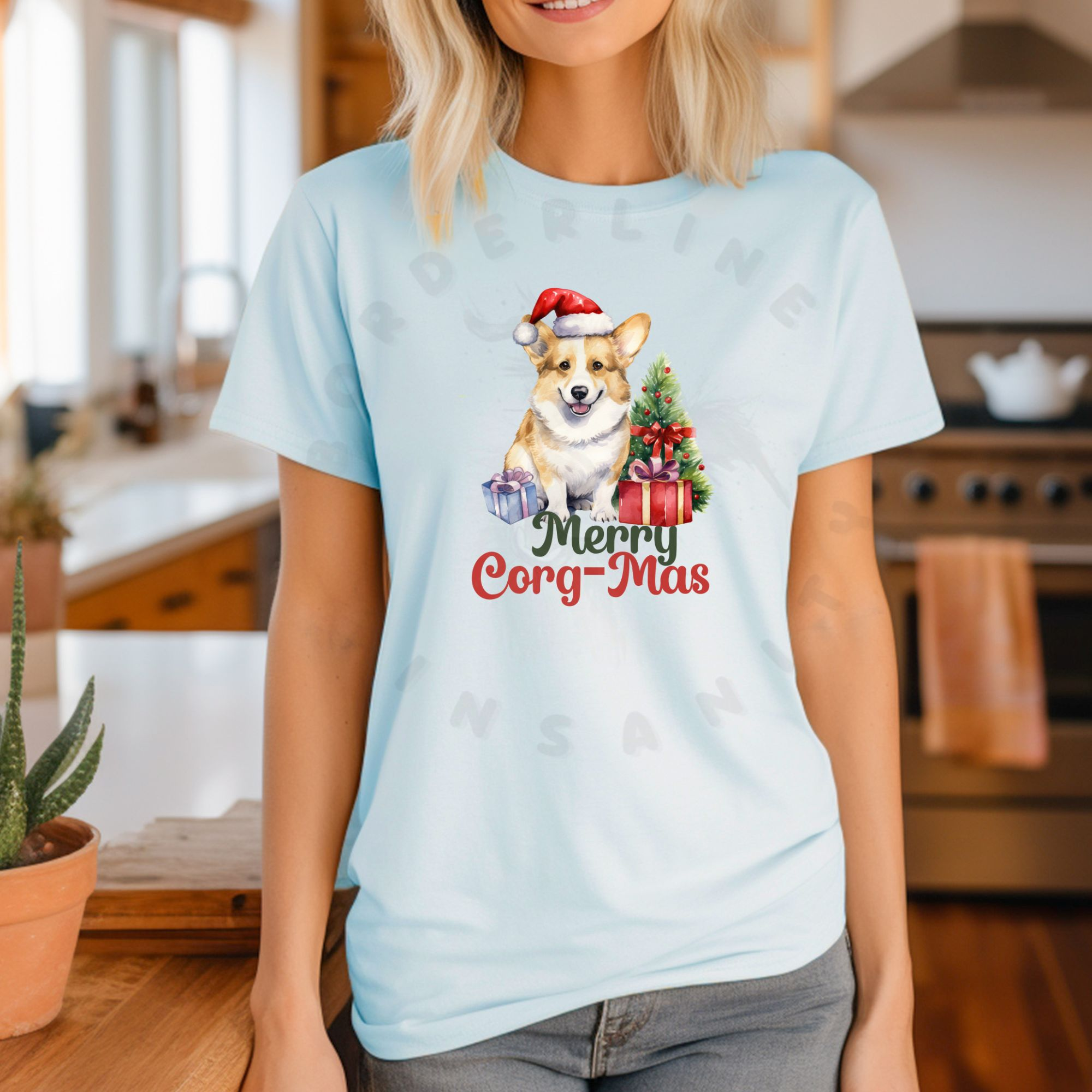 a woman standing in a kitchen wearing a heather ice blue t-shirt with a graphic of a corgi in a santa hat with a christmas tree and gifts that says Merry Corg-mas