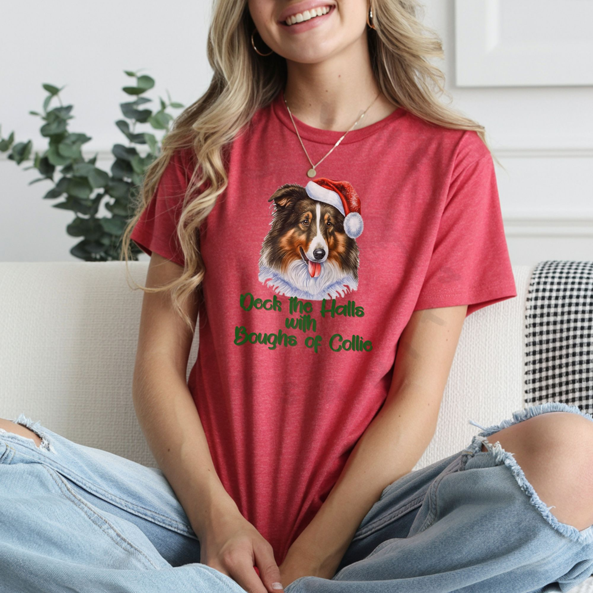 a woman wearing ripped jeans sitting on a sofa wearing a heather red t-shirt that features a rough collie wearing a santa hat and says Deck the halls with boughs of collie