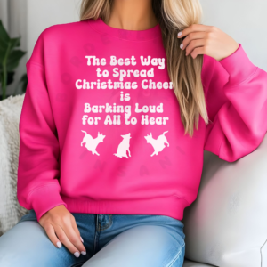 a woman sitting on a couch wearing a bright pink sweatshirt that says the best way to spread christmas cheer is barking loud for all to hear with 3 barking dog silhouettes underneath