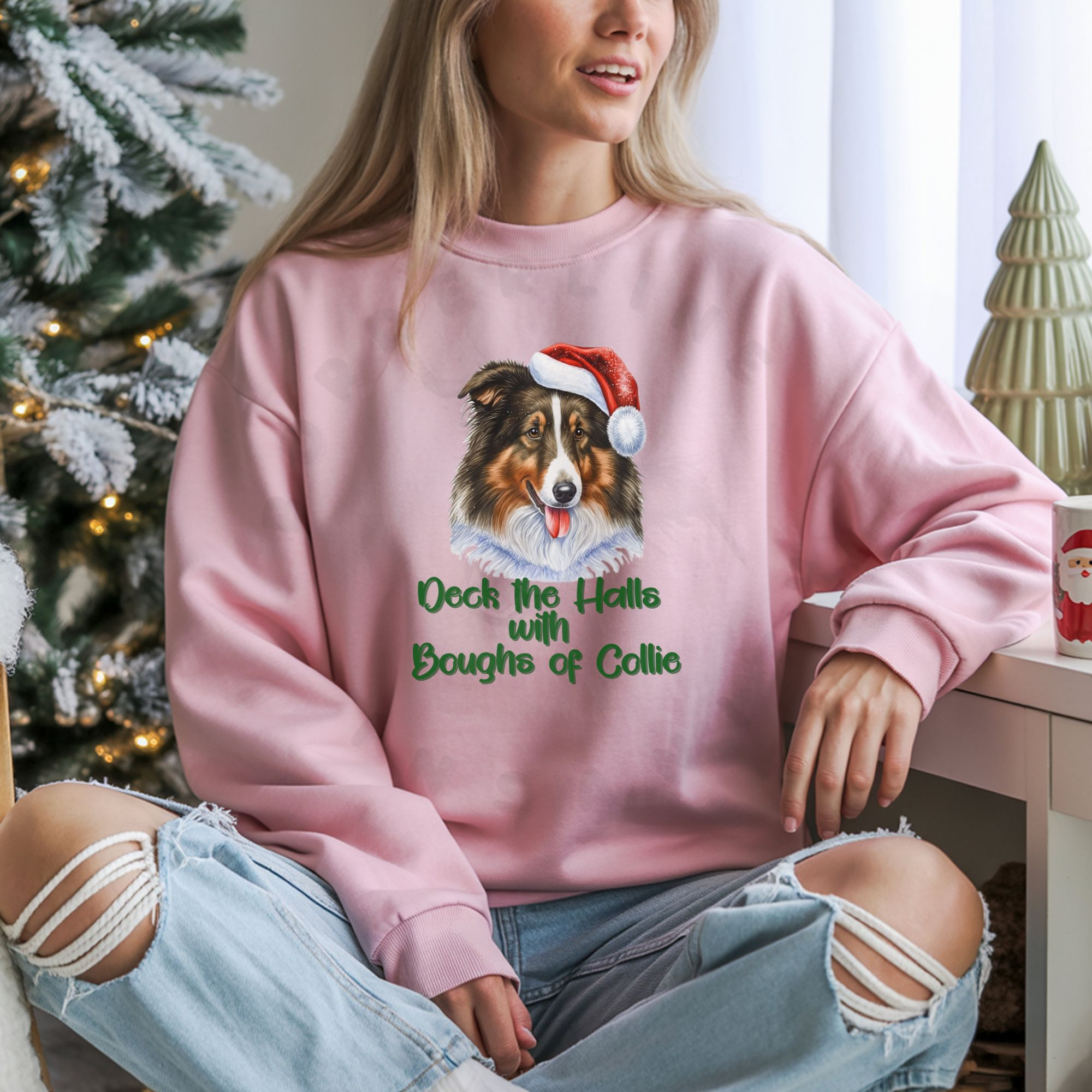 a woman sitting on a sofa wearing a light pink sweatshirt with a rough collie in a santa hat and the words deck the halls with boughs of collie