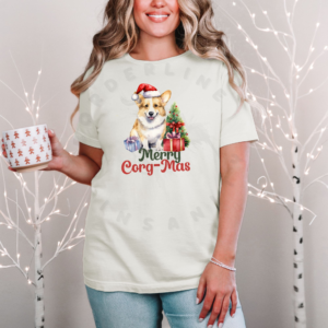 a woman standing in front of a christmas background holding a festive mug wearing an ivory (natural) t-shirt with a graphic of a corgi in a Santa hat with a Christmas tree and gifts that says Merry Corg-mas