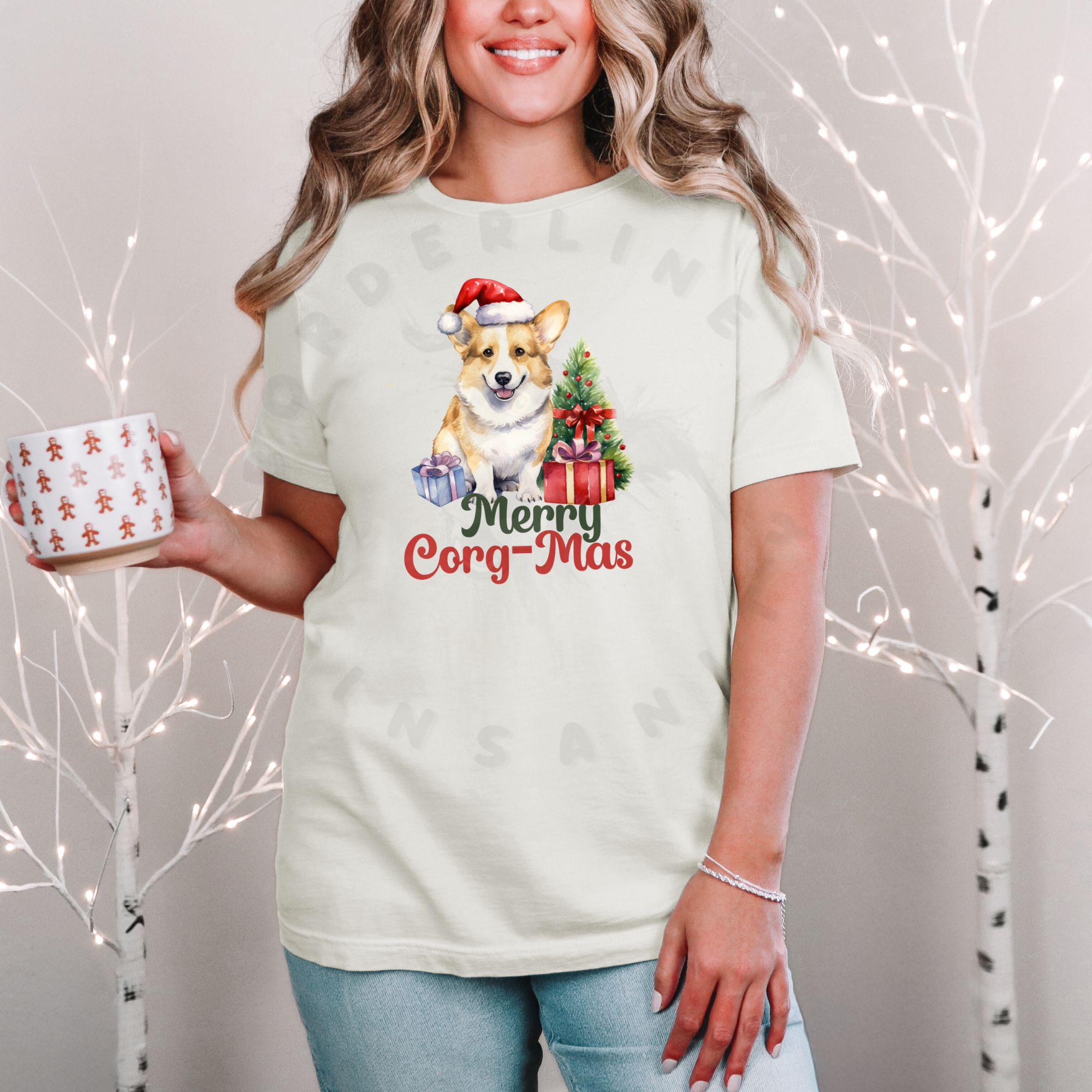 a woman standing in front of a christmas background holding a festive mug wearing an ivory (natural) t-shirt with a graphic of a corgi in a Santa hat with a Christmas tree and gifts that says Merry Corg-mas