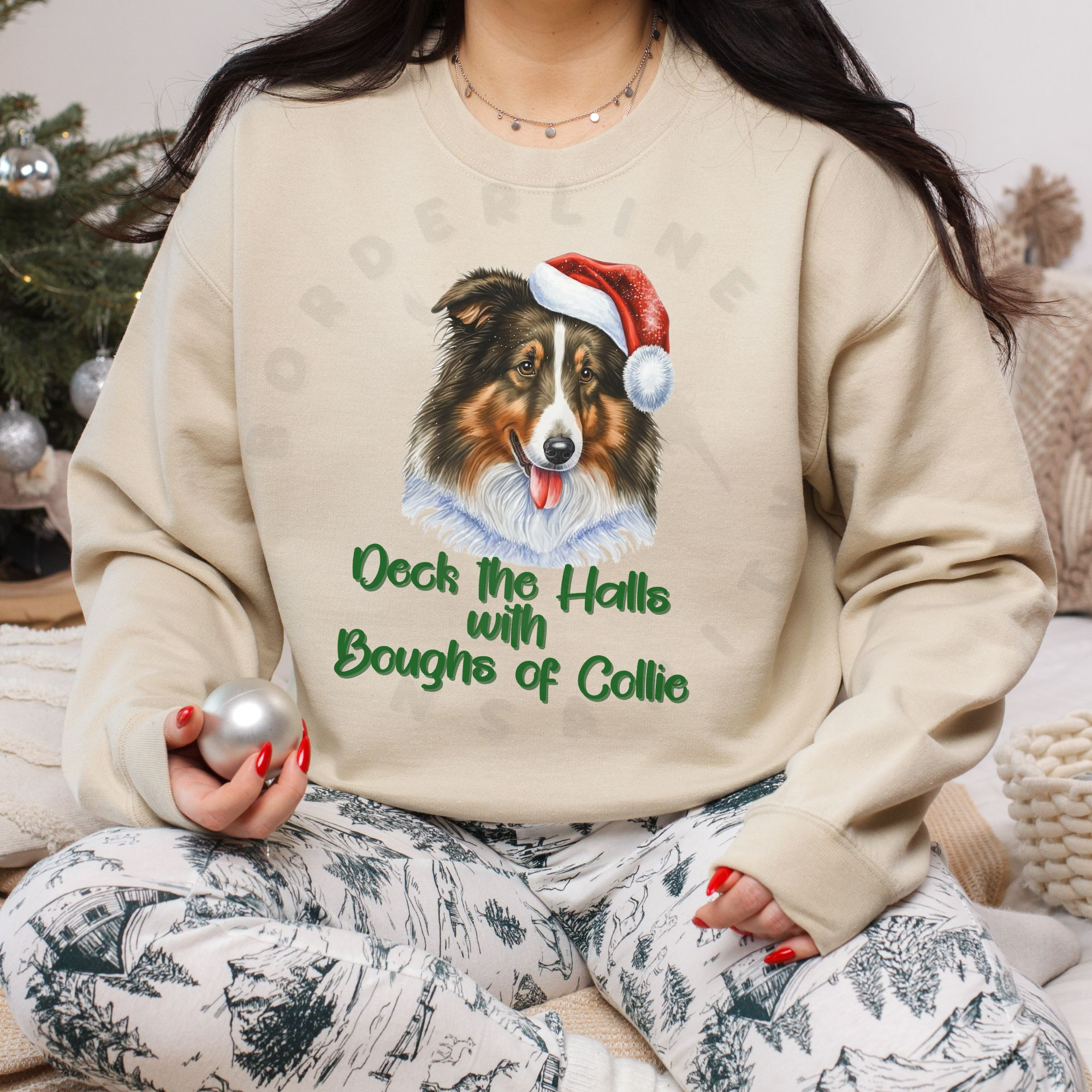 a woman sitting among christmas decorations with an ornament in her hand wearing a sand sweatshirt with a rough collie in a santa hat and the words deck the halls with boughs of collie