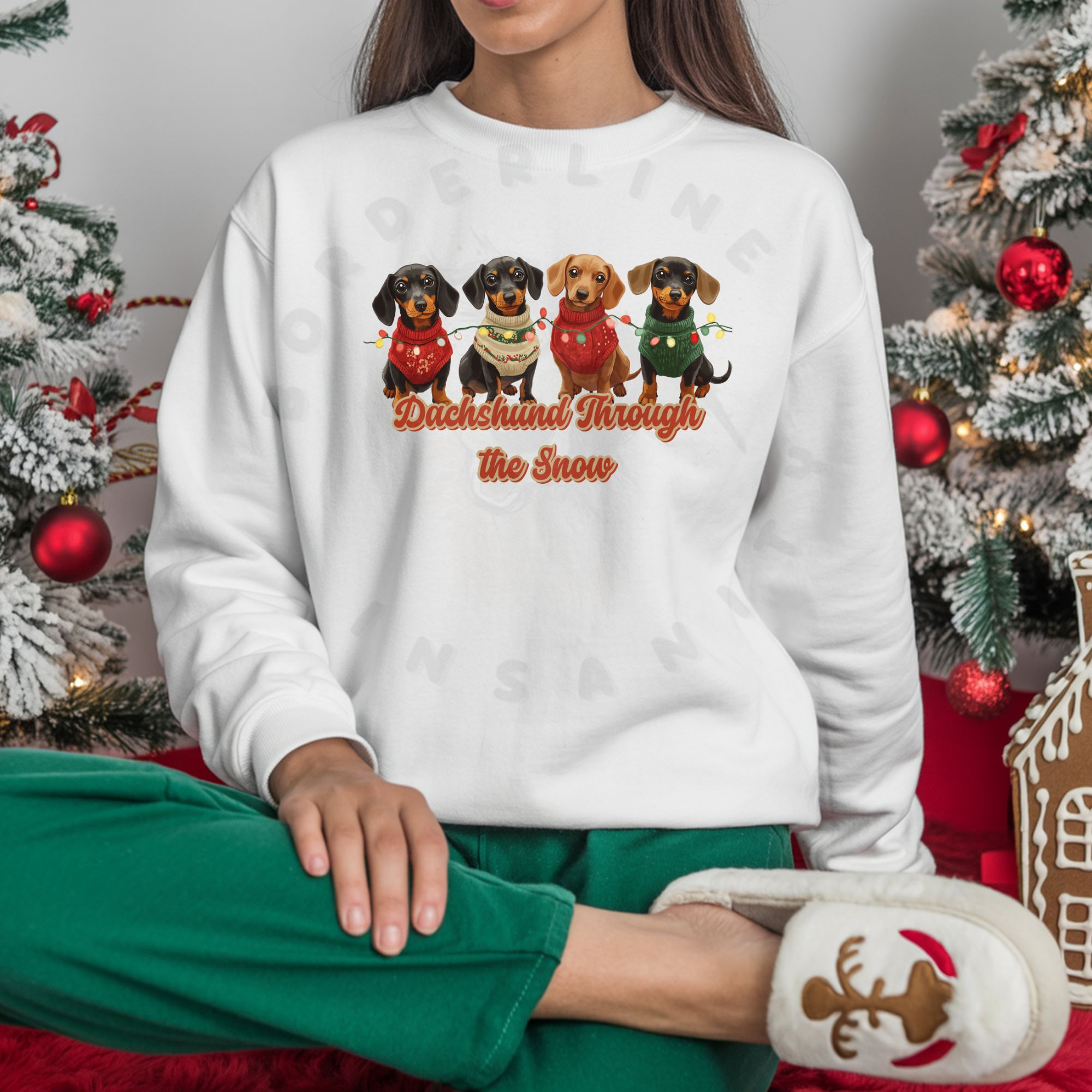 a woman sitting between 2 christmas trees wearing a white dachshund through the snow sweatshirt featuring 4 dachshunds wearing christmas sweaters and tangled in christmas lights