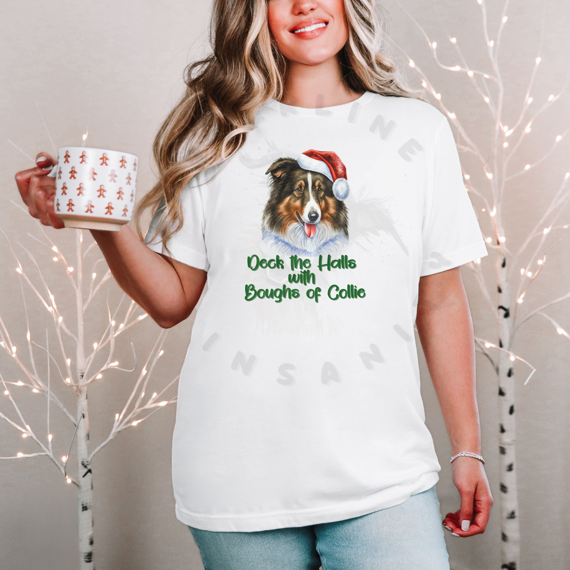 a woman standing in front of a christmas background holding a holiday mug wearing a white t-shirt that features a rough collie wearing a santa hat and says Deck the halls with boughs of collie