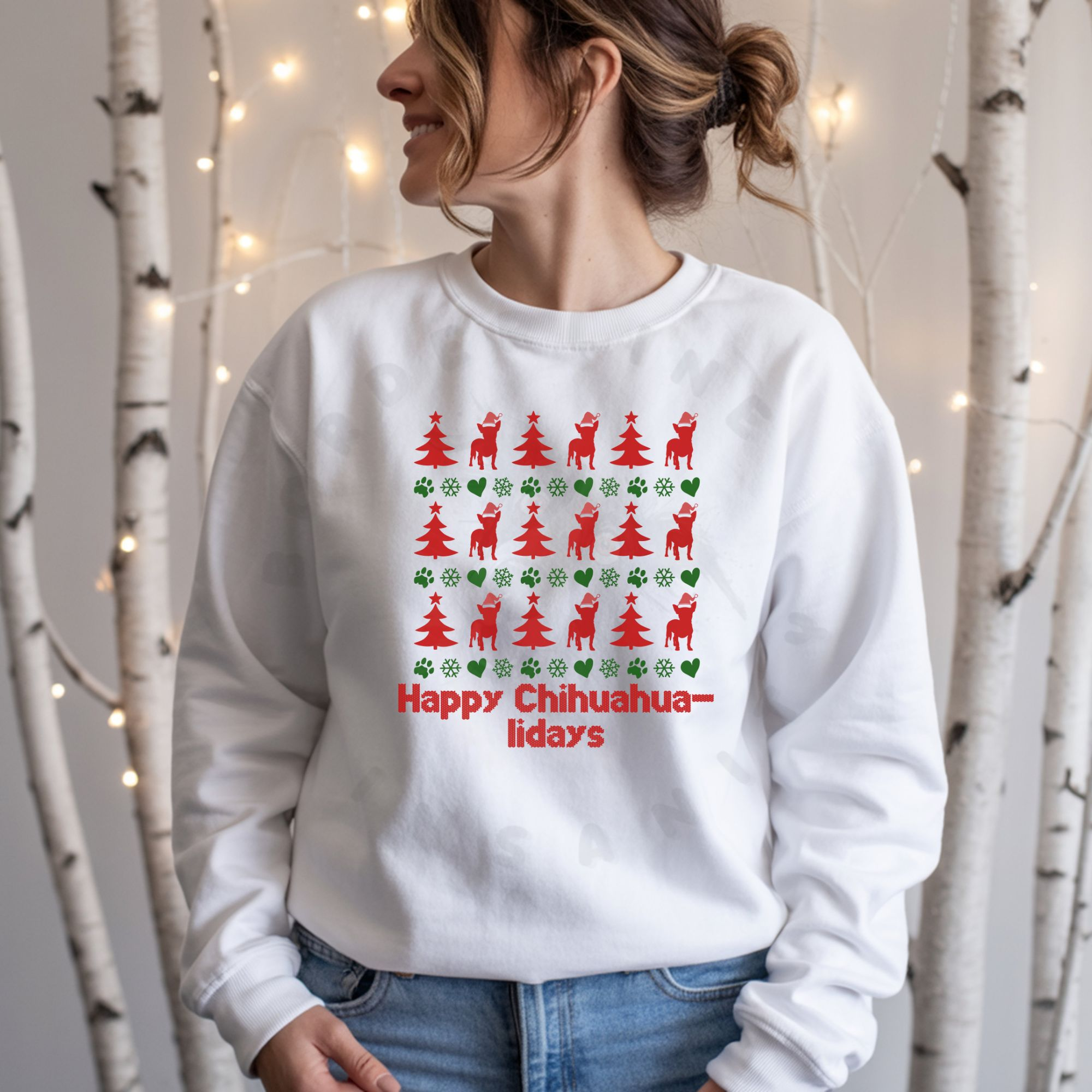 a woman standing in front of white christmas lights and birch tree trunks wearing a white sweatshirt designed ugly christmas sweater style with rows of red christmas trees, green snowflakes, and chihuahuas wearing santa hats.