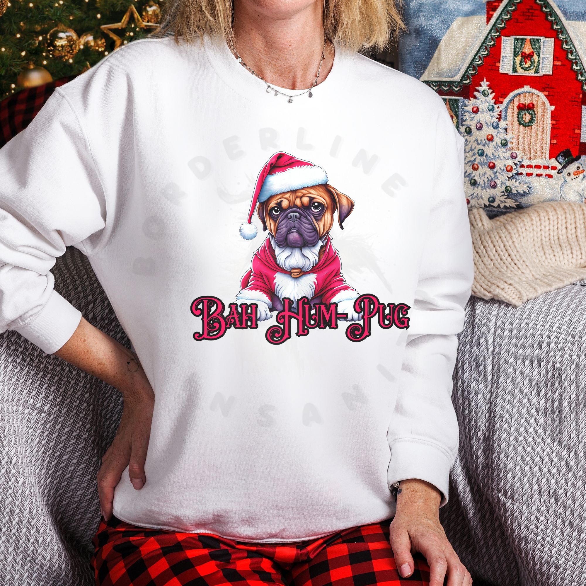 a woman sitting on a sofa wearing a white sweatshirt that says bah hum-pug below a graphic of a grumpy pug wearing a santa suit