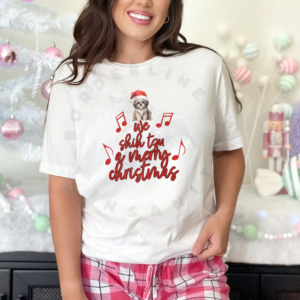 a woman in pink plaid pajama pants in front of a pastel christmas background wearing a white tee featuring a shih tzu in a santa hat at the top of the phrase we shih tzu a merry christmas