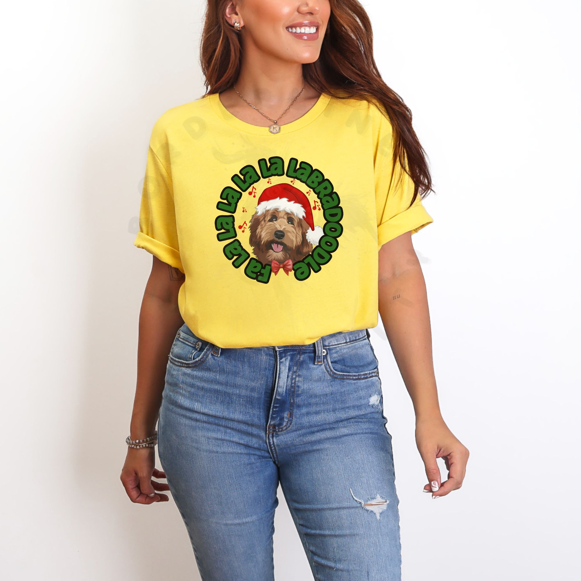 a woman standing in front of a white background wearing a yellow tee featuring a graphic of a labradoodle wearing a santa hat and the words Fa la la la la la labradoodle