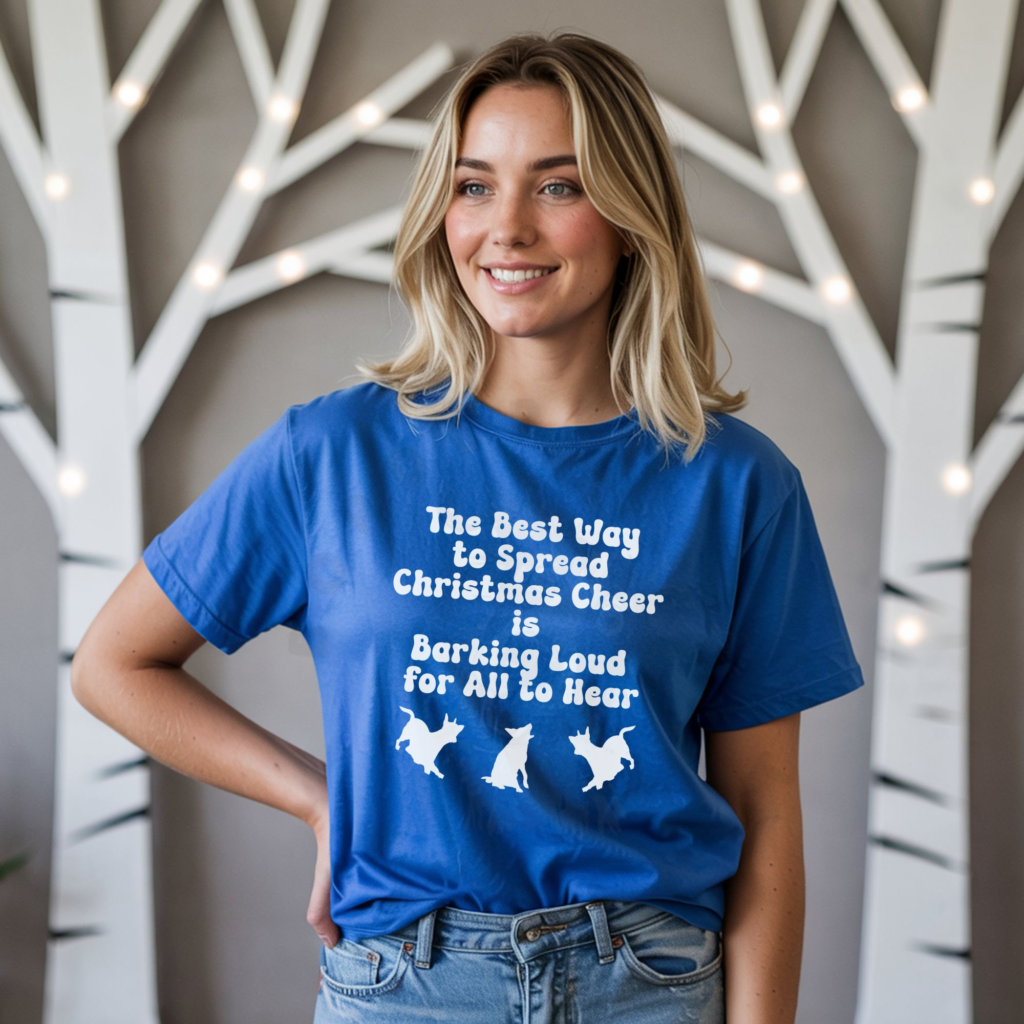 a woman standing in front of lighted birch trees wearing a royal blue tee that says the best way to spread christmas cheer is barking loud for all to hear with 3 barking dog silhouettes underneath