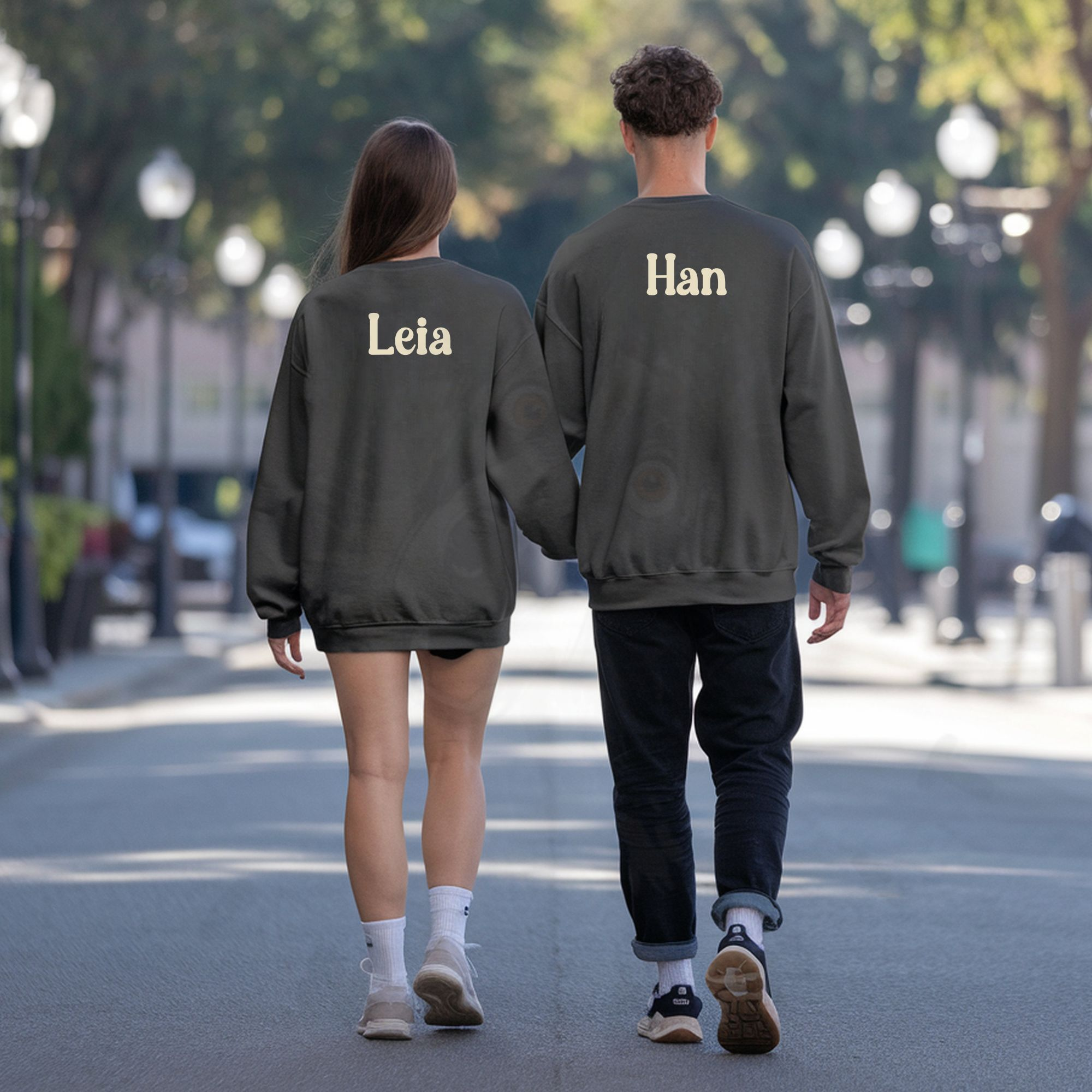 a man & woman walking down the street facing away from the camera wearing charcoal grey sweatshirts that say their names on the back