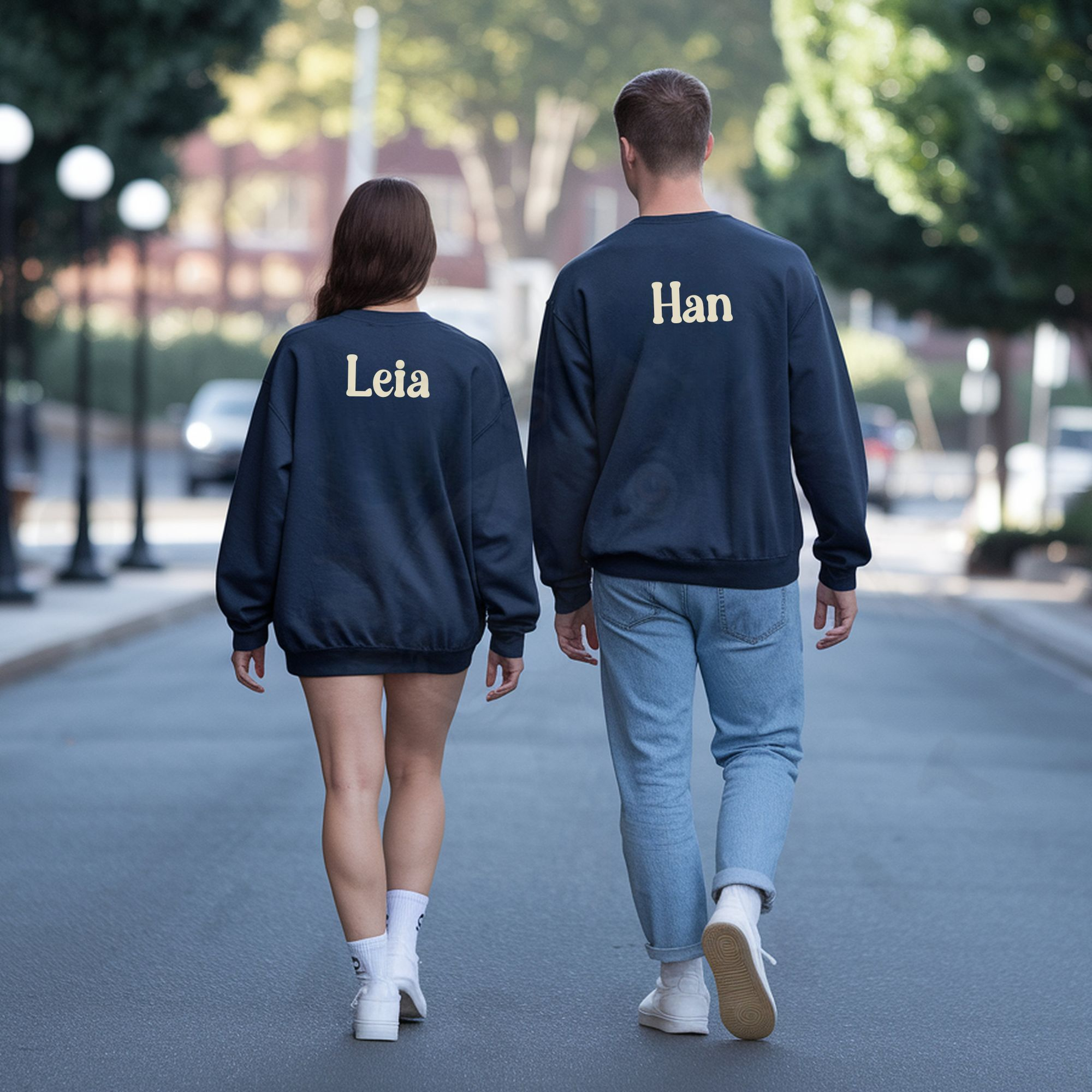 a man and woman facing away from the camera and walking down the street wearing navy blue sweatshirts that say their names on the back
